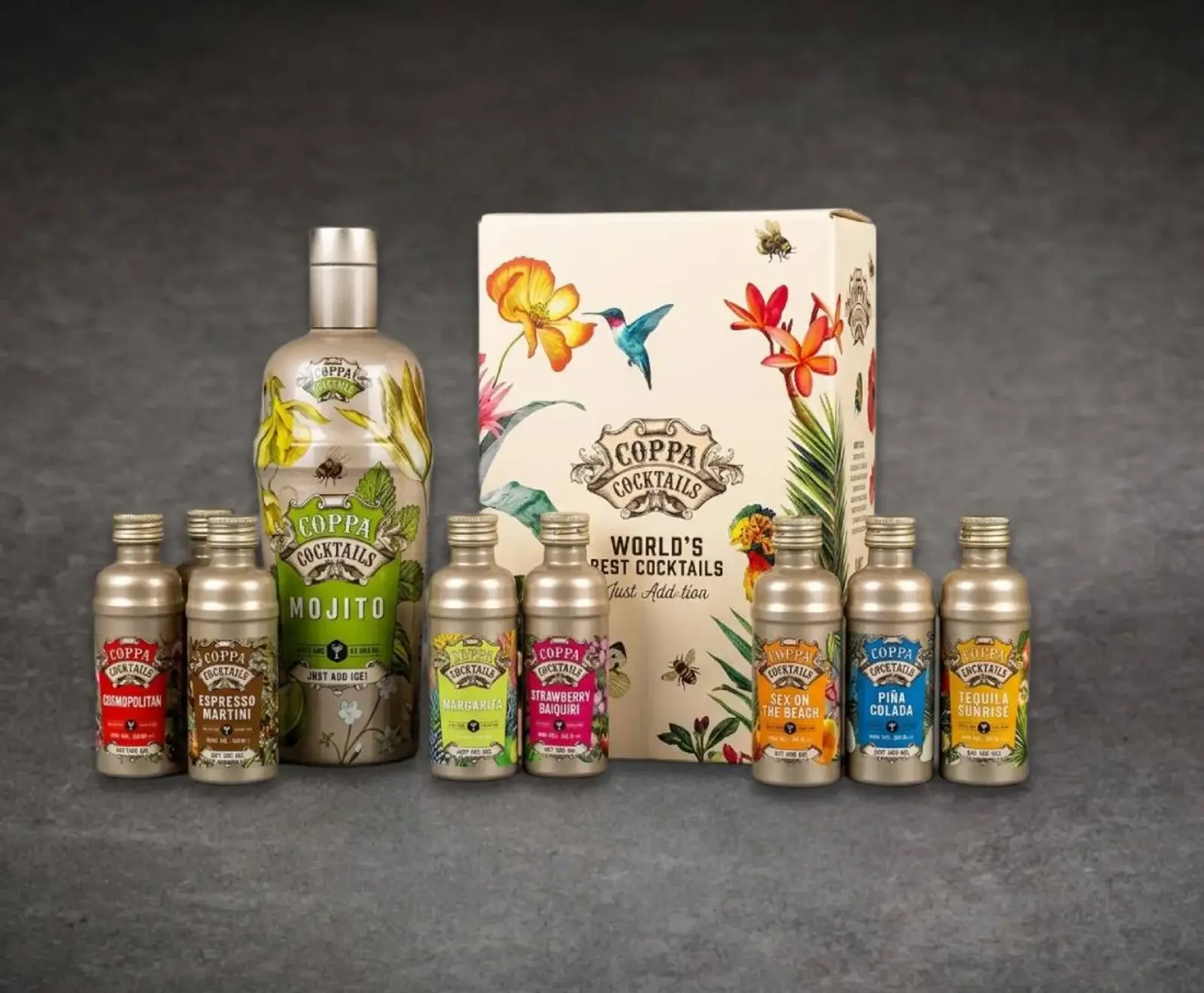 Eine große Flasche Coppa Mojito, eine Geschenkbox mit tropischem Design und sieben kleine Flaschen verschiedener Coppa Cocktails (Cosmopolitan, Espresso Martini, Margarita, Strawberry Daiquiri, Sex on the Beach, Piña Colada, Tequila Sunrise) auf grauem