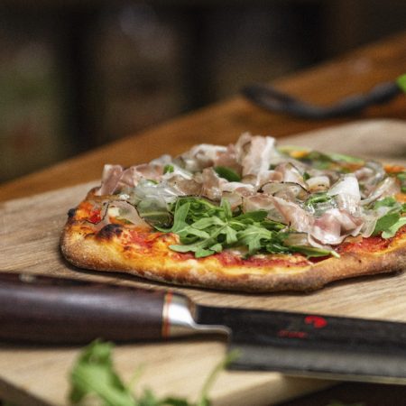 Knusprige Pizza vom Grill belegt mit Schinken und Rucola