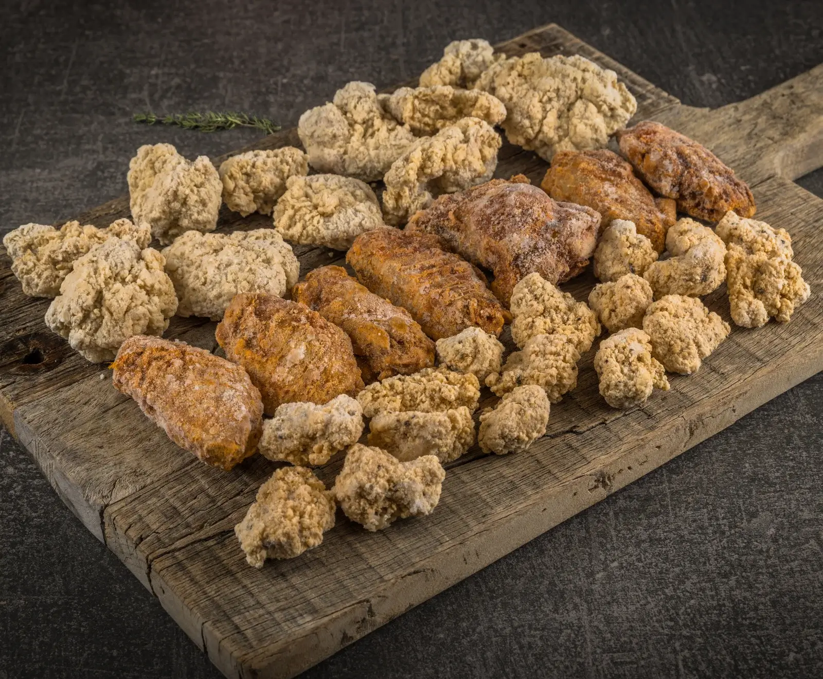 Eine Mischung aus gefrorenen, panierten Hähnchenflügeln und Nuggets auf einem rustikalen Holzbrett, mit einem Thymianzweig im Hintergrund.