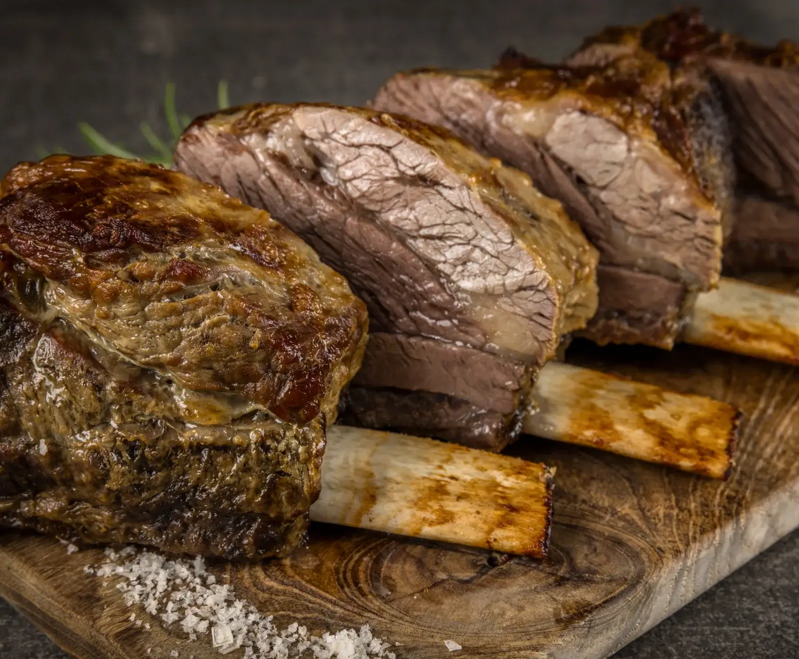 Gegrillte oder geschmorte Rinderrippen, in Scheiben geschnitten, auf einem Holzbrett mit grobem Meersalz und Rosmarin. Das Fleisch ist außen knusprig braun und innen zart.