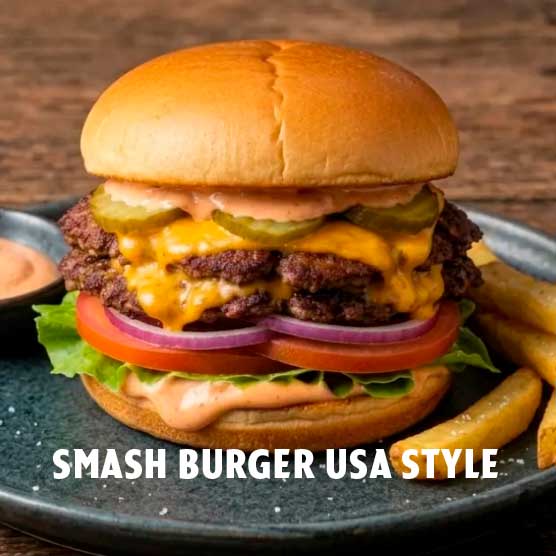 Ein doppelter Smash Burger mit geschmolzenem Käse, Gewürzgurken, Salat, Tomate, roten Zwiebeln und Spezialsoße auf einem Brötchen, serviert mit Pommes frites und Dip auf einem dunklen Teller.