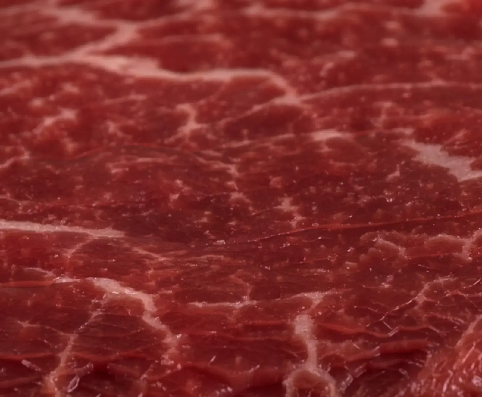 Nahaufnahme von rotem Rindfleisch mit ausgeprägter weißer Marmorierung, die ein feines Netzmuster bildet. Die Textur des rohen Fleisches ist detailliert sichtbar.