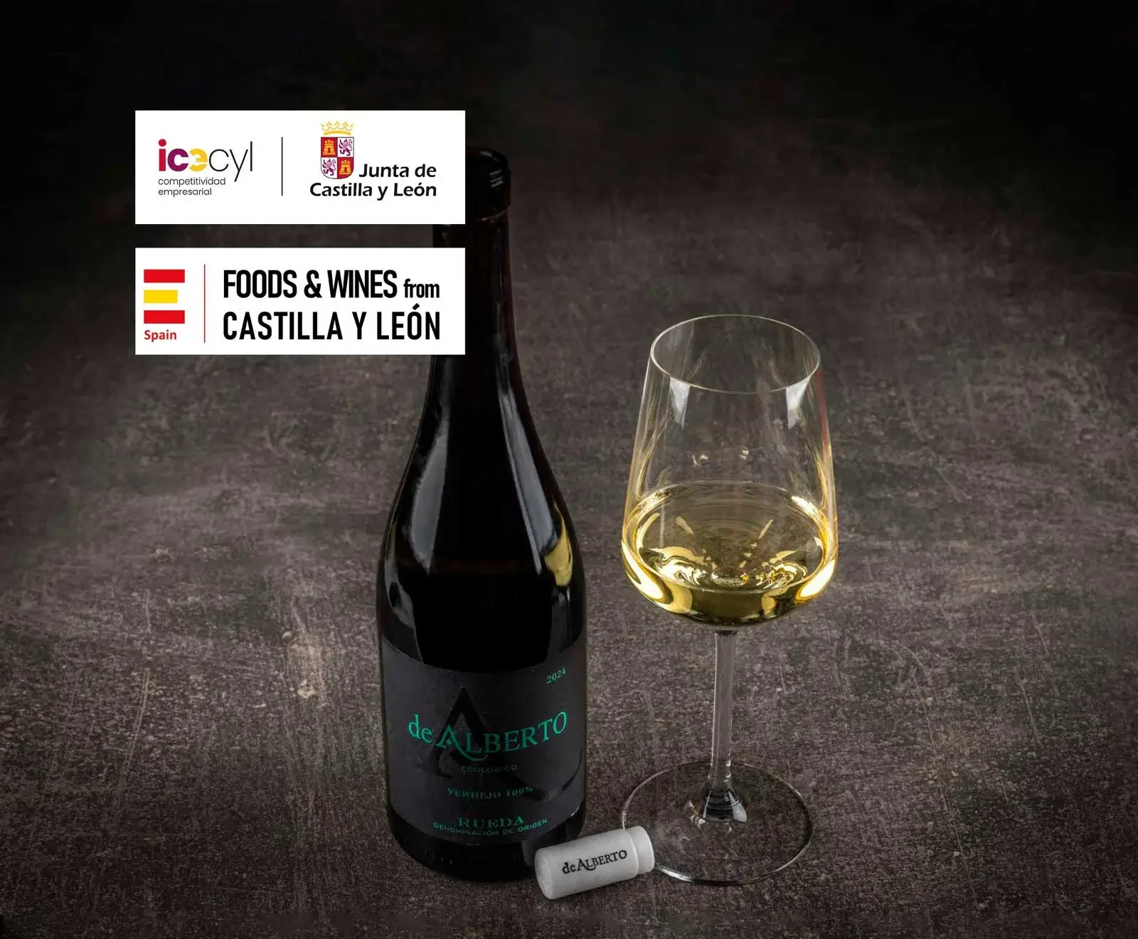 Flasche 'de ALBERTO' Verdejo Weißwein aus Rueda mit schwarzem Etikett und ein gefülltes Weinglas auf dunklem Untergrund. Oben links Logos von Castilla y León und 'Foods & Wines from Castilla y León'.
