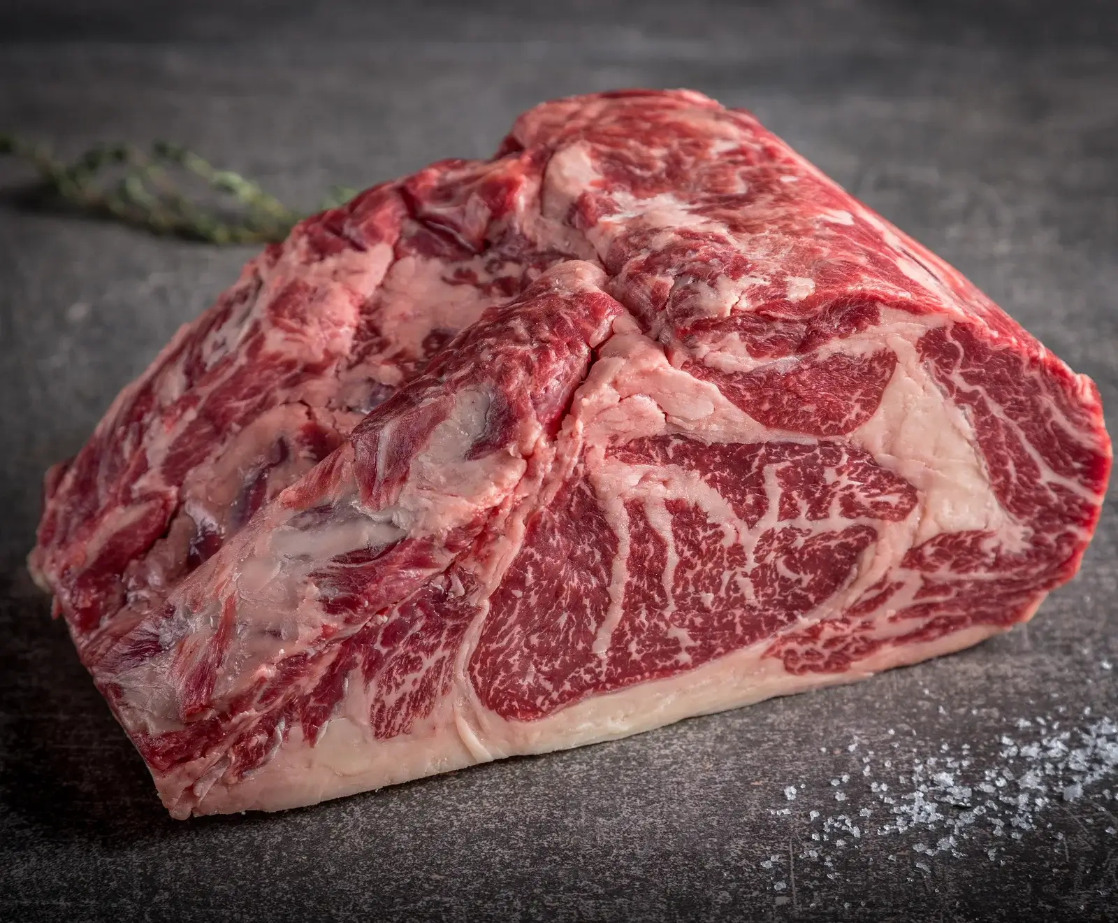 Rohes Rindfleisch-Steak mit sichtbaren Fettadern auf dunklem Hintergrund, bestreut mit Salz