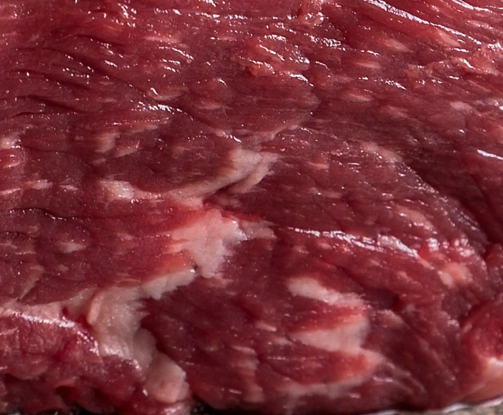 Nahaufnahme von rohem, dunkelrotem Fleisch mit deutlicher weißer Fettmarmorierung. Die Oberfläche glänzt leicht und zeigt feine Muskelfasern.