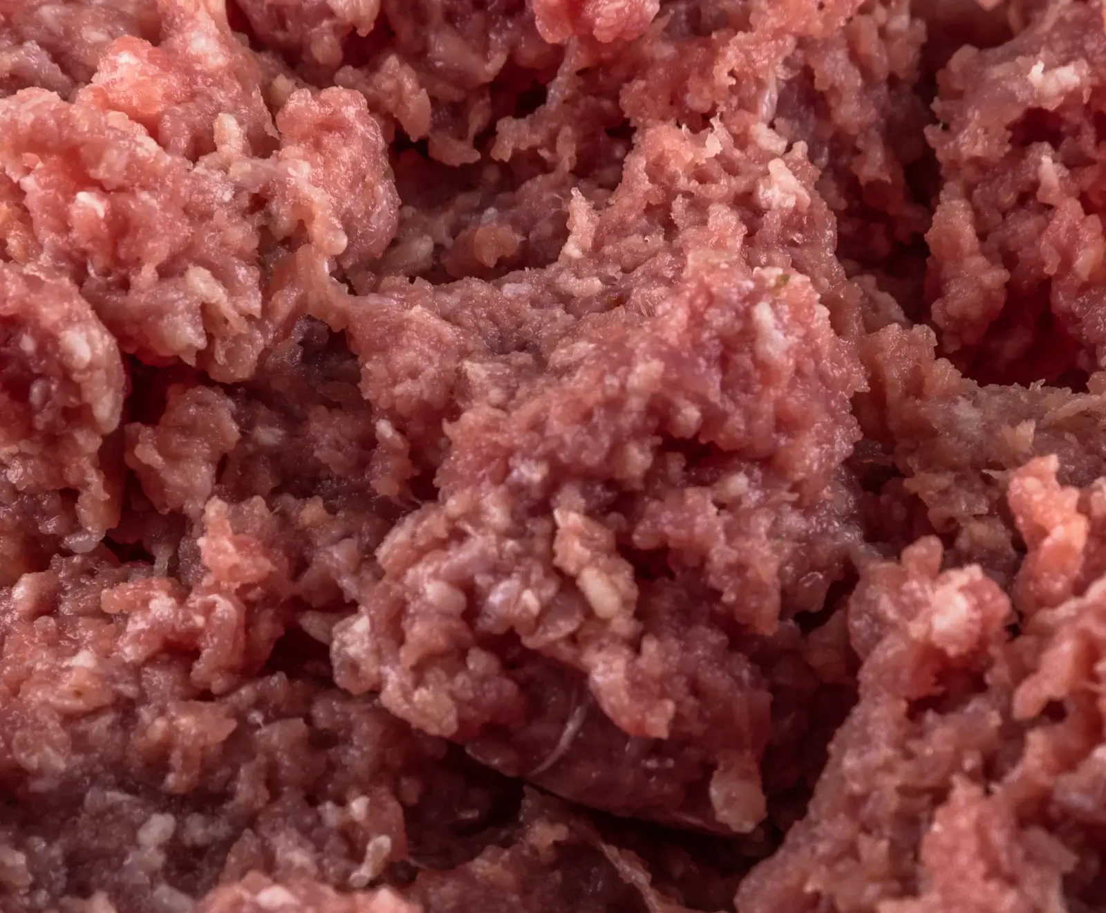 Nahaufnahme von rohem, rosa Hackfleisch mit sichtbaren Fettstücken, das eine unregelmäßige, körnige Textur aufweist.