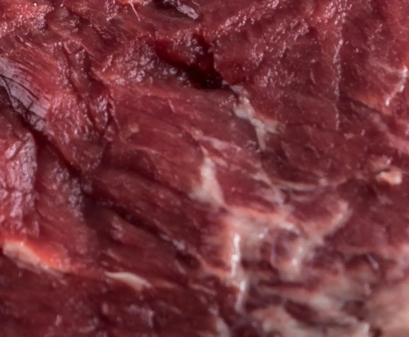 Nahaufnahme von rotem rohem Fleisch mit sichtbaren Muskelfasern und feinen weißen Fettadern, die eine faserige Textur und leichte Marmorierung zeigen.