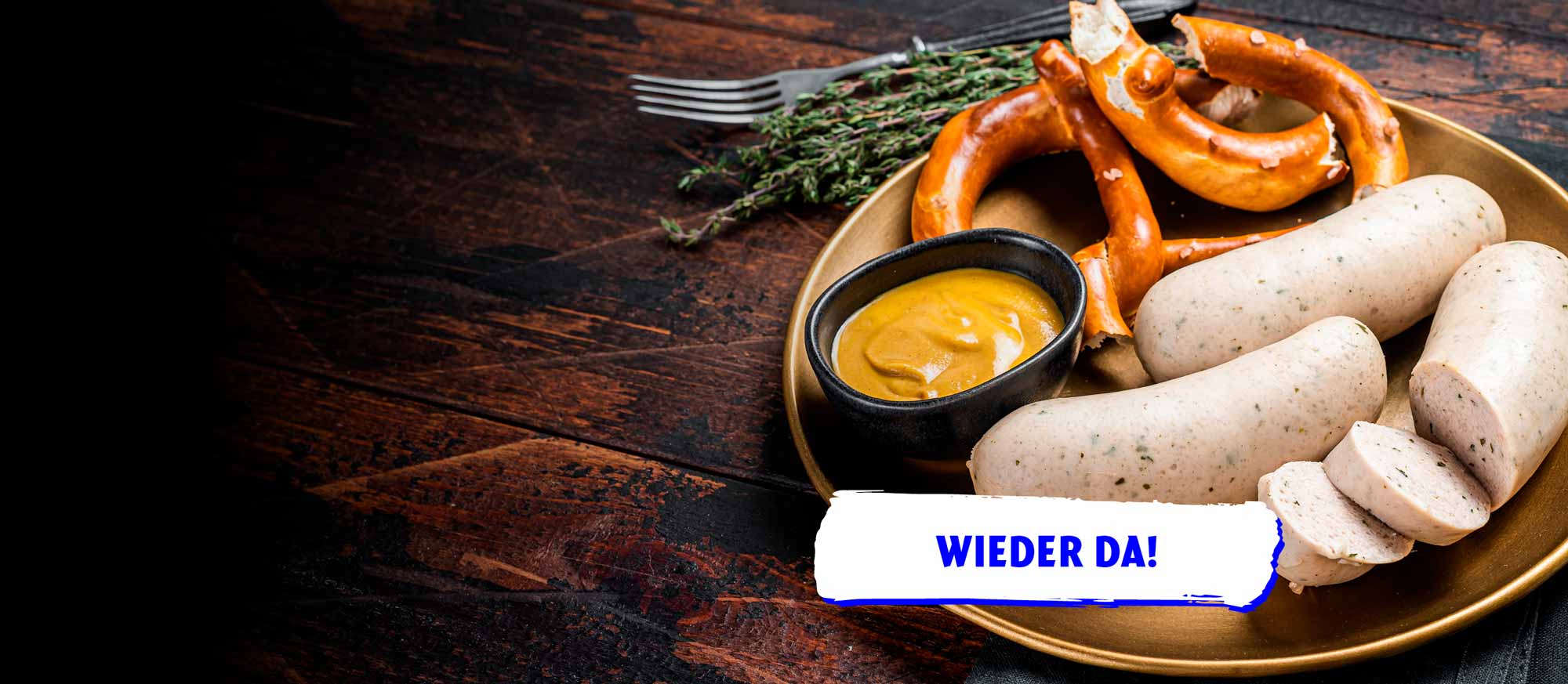 Eine goldene Platte mit Weißwürsten, Brezeln und Senf auf einem dunklen Holztisch, garniert mit Thymian. Ein Banner mit der Aufschrift "WIEDER DA!" ist unten rechts eingeblendet.