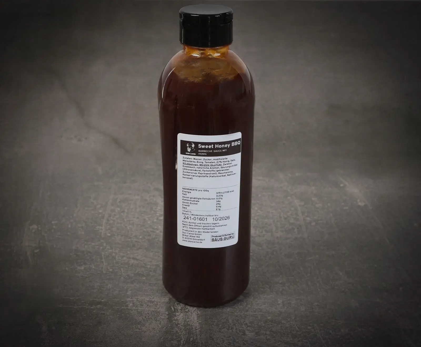 Eine braune Flasche Don Carne Sweet Honey BBQ Sauce mit schwarzem Klappdeckel, stehend auf dunklem Untergrund. Das weiße Etikett mit Zutaten, Nährwerten und dem Namen ist gut lesbar.