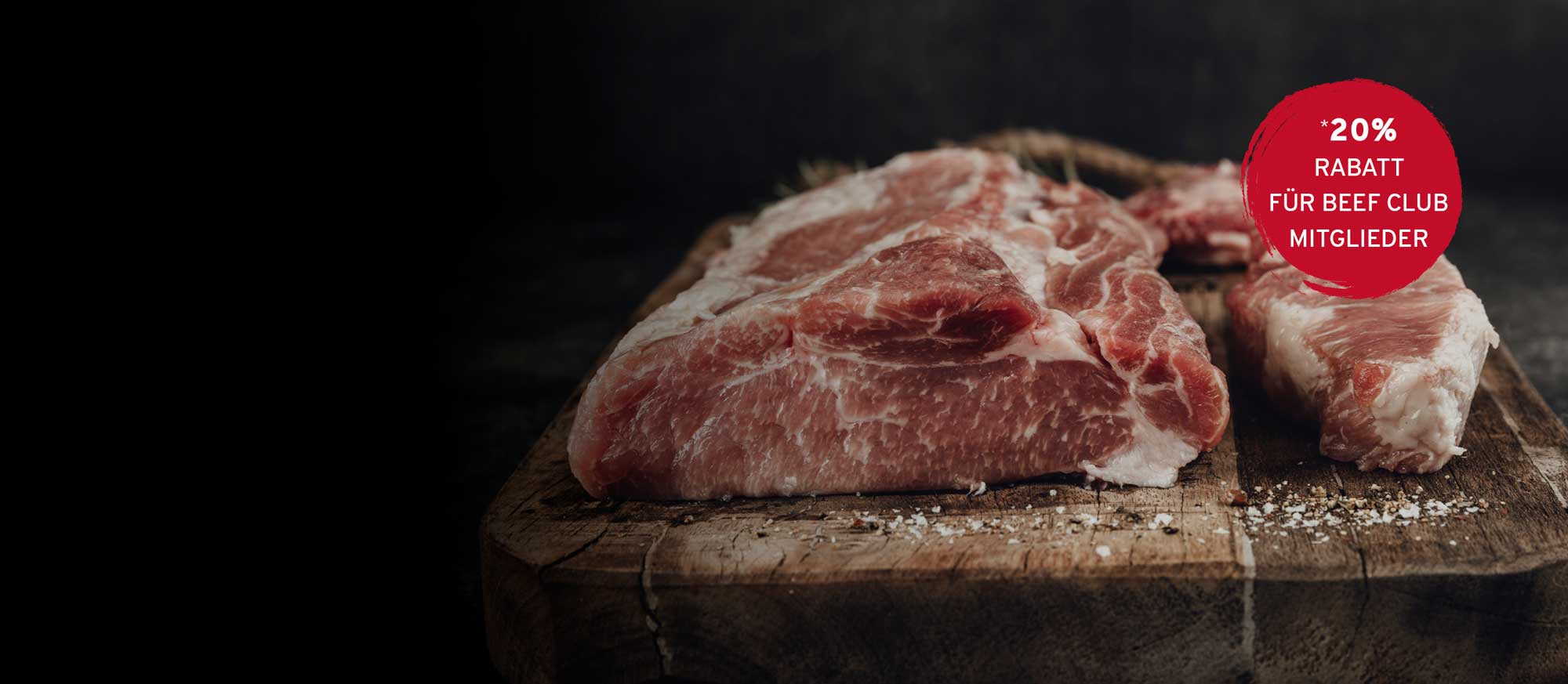 Rohe Fleischstücke auf rustikalem Holzbrett mit Salz und Pfeffer. Roter Kreis mit Text: *20% RABATT FÜR BEEF CLUB MITGLIEDER.