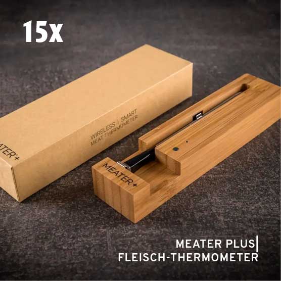 Ein MEATER+ kabelloses Smart-Fleischthermometer in seiner hölzernen Ladestation. Im Hintergrund ist die braune Produktverpackung sichtbar. Die Texte "15x" und "MEATER PLUS | FLEISCH-THERMOMETER" sind eingeblendet.