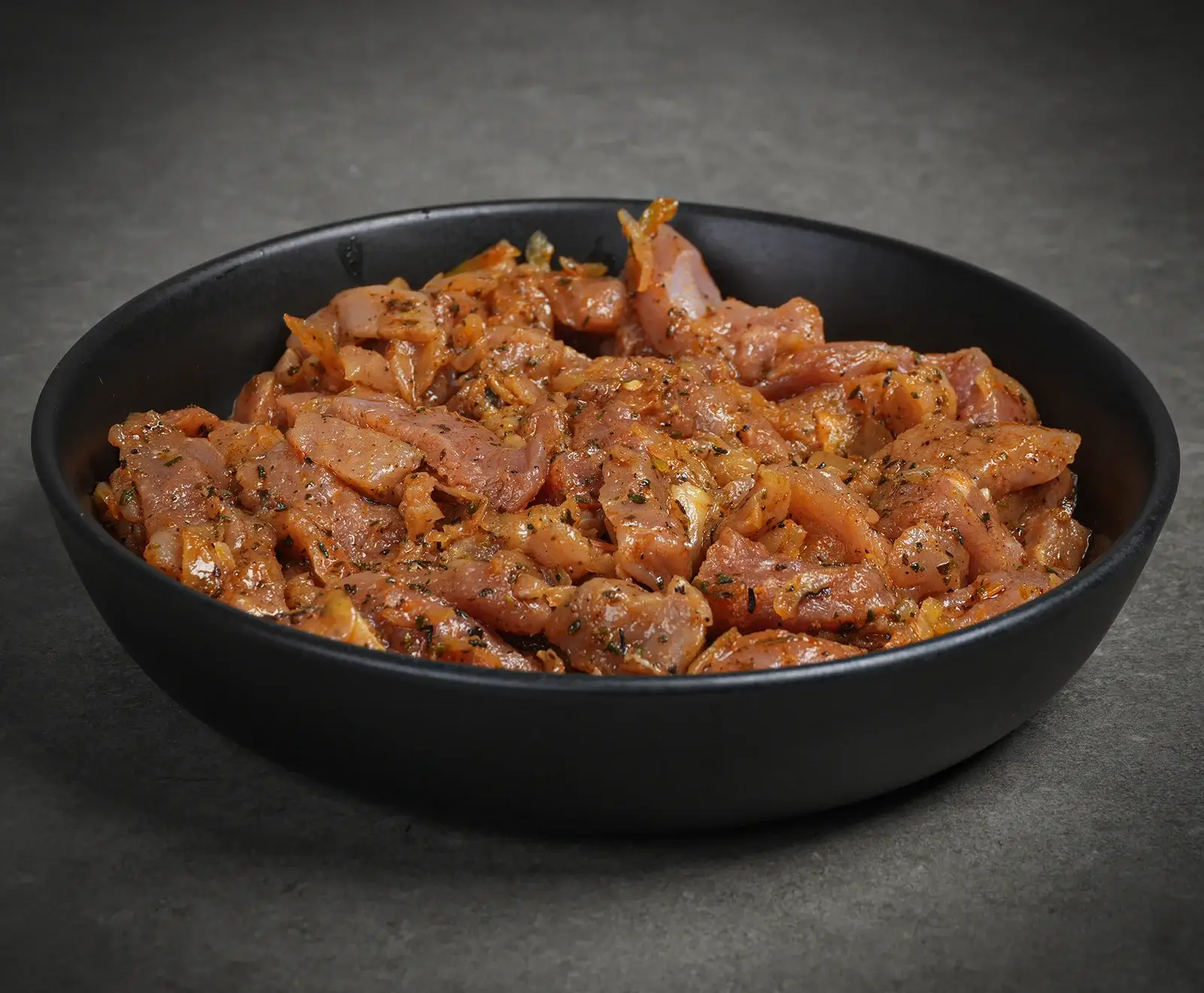 Rohes, in Streifen geschnittenes Fleisch, mariniert in einer würzigen Soße mit Kräutern, in einer schwarzen Schale auf grauem Hintergrund.