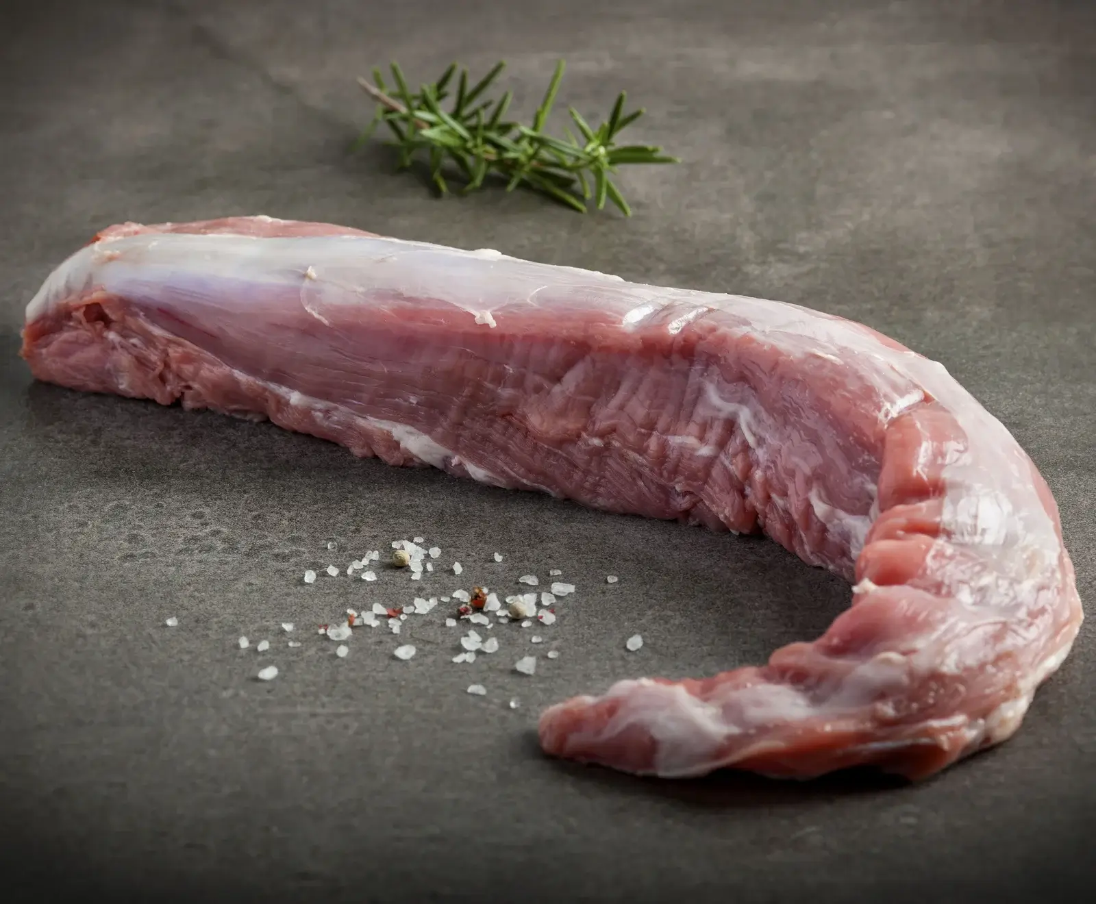 Rohes Schweinefleisch, gewürzt mit Salz und Rosmarin, auf dunklem Hintergrund