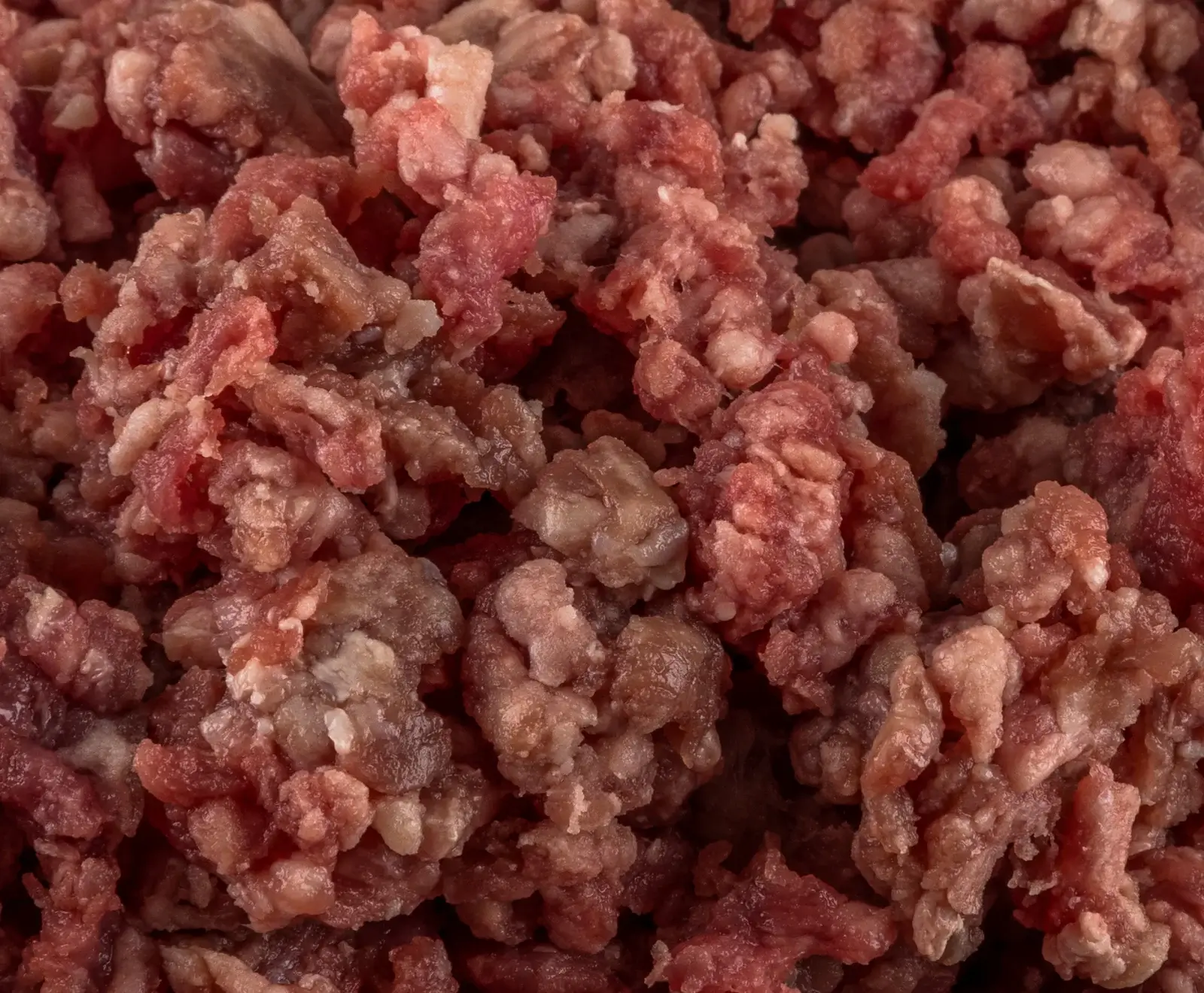 Nahaufnahme von rohem, grob gehacktem Fleisch, bestehend aus roten Muskelfasern und helleren Fettstücken. Die Oberfläche wirkt feucht und hat verschiedene Rosa- und Rottöne.