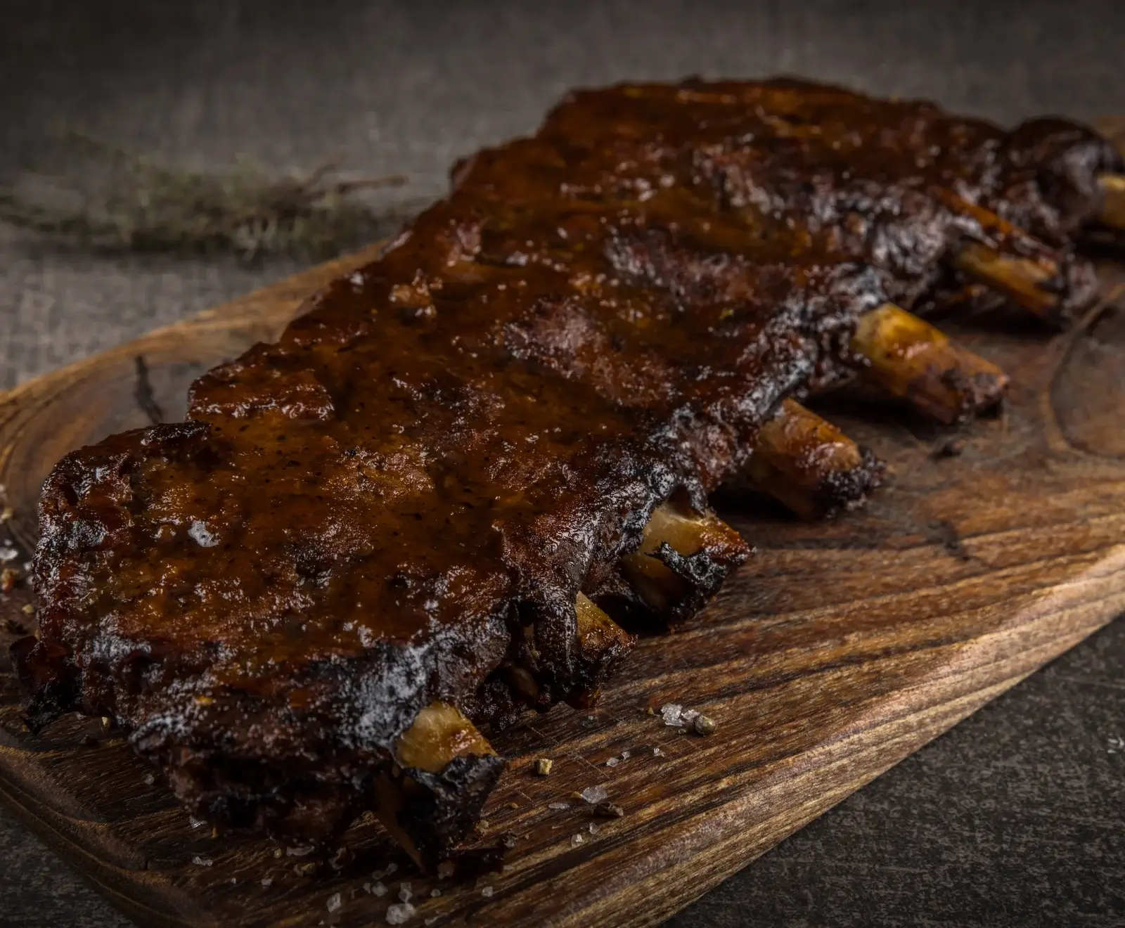 Zwei gegrillte, barbecue-glasierte Spareribs auf einem rustikalen Holzbrett