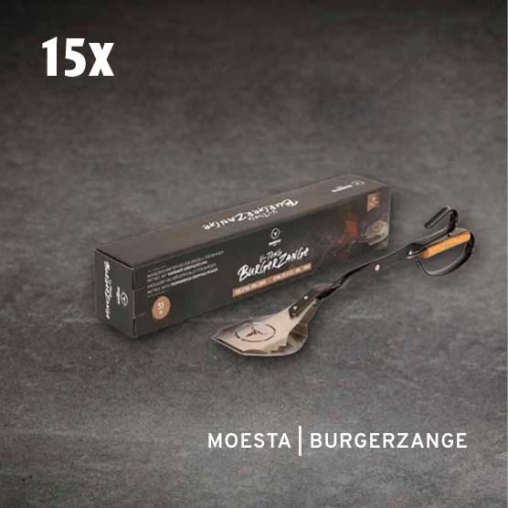 15x Moesta Burgerzange: Eine schwarze Produktverpackung und eine silberne Burgerzange mit Holzgriff liegen auf einem dunklen, strukturierten Untergrund. Die Zange kombiniert Spatel und Greifzange.