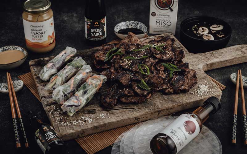 Leckeres Steak-Dinner mit asiatischen Aromen Gegrilltes Steak mit Frühlingszwiebeln auf Holzbrett, umgeben von asiatischen Saucen und Beilagen.