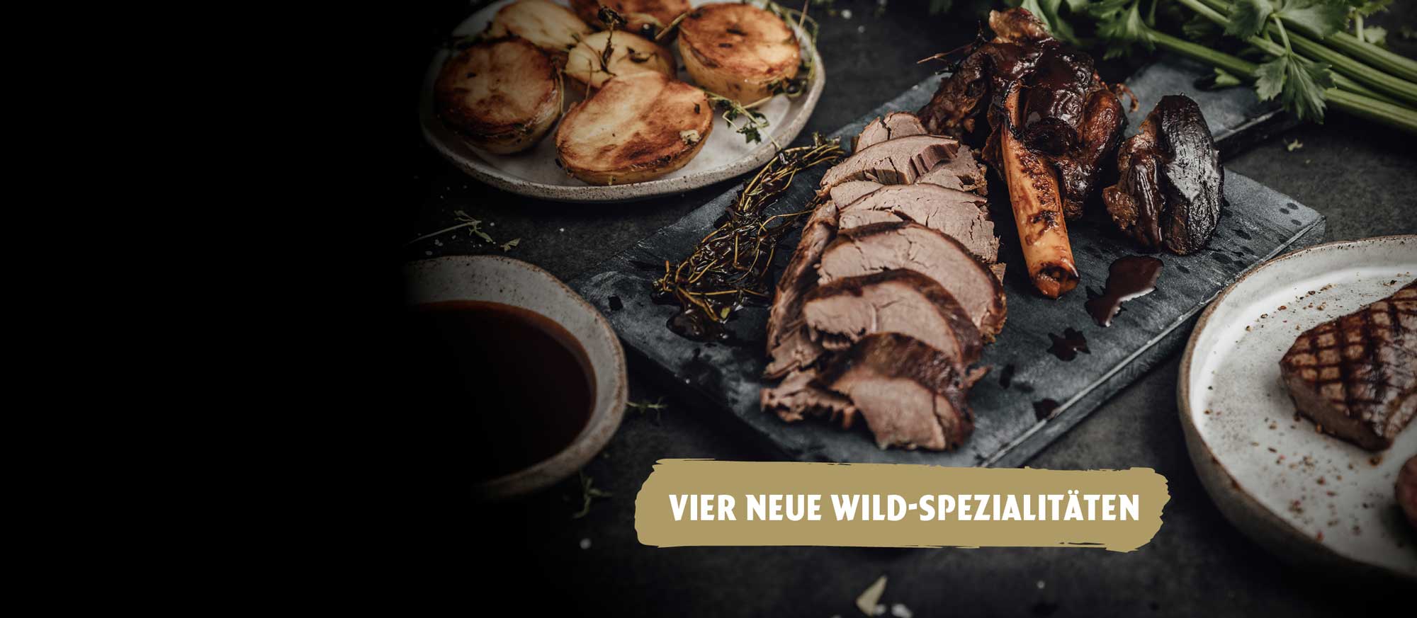 Eine dunkle Aufnahme von verschiedenen Wildgerichten: geschnittenes Wildbraten, ein Knochenstück, ein Steak, Bratkartoffeln und Sauce. Im Vordergrund der Text: VIER NEUE WILD-SPEZIALITÄTEN.