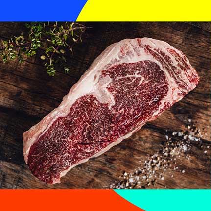 Rohes Ribeye-Steak mit starker Marmorierung auf dunklem Holzbrett, garniert mit frischem Thymian und grobem Salz.