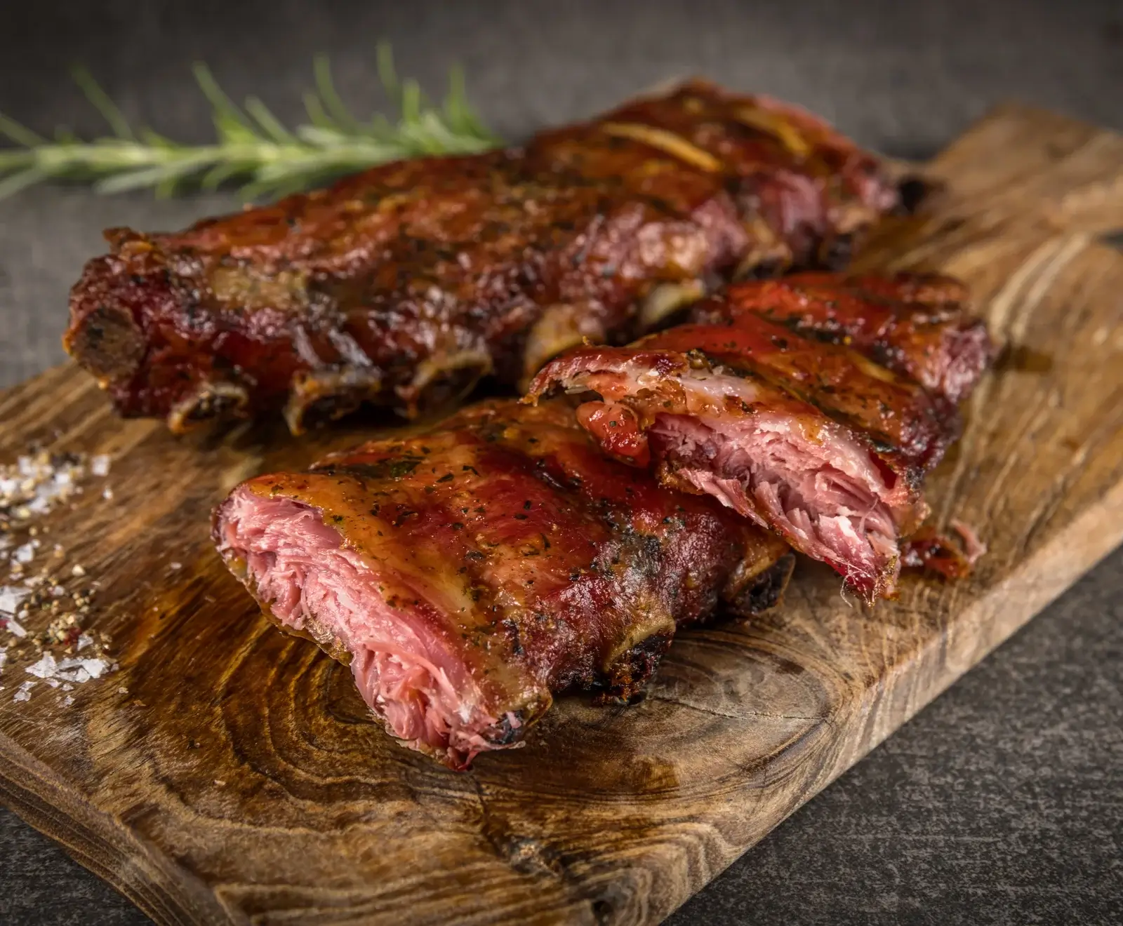 Saftige, gebratene Rippchen mit knuspriger Kruste und Rosmarin auf einem Holzbrett serviert.