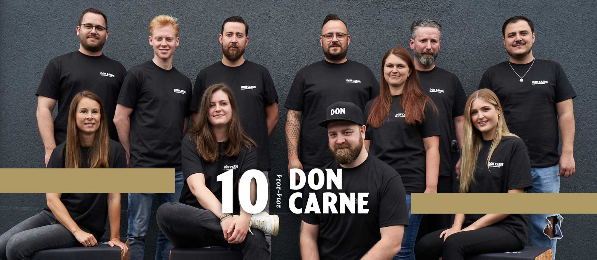 Das Team von Don Carne vor einer grauen Wand mit 10 Jahre Logo und Banderole