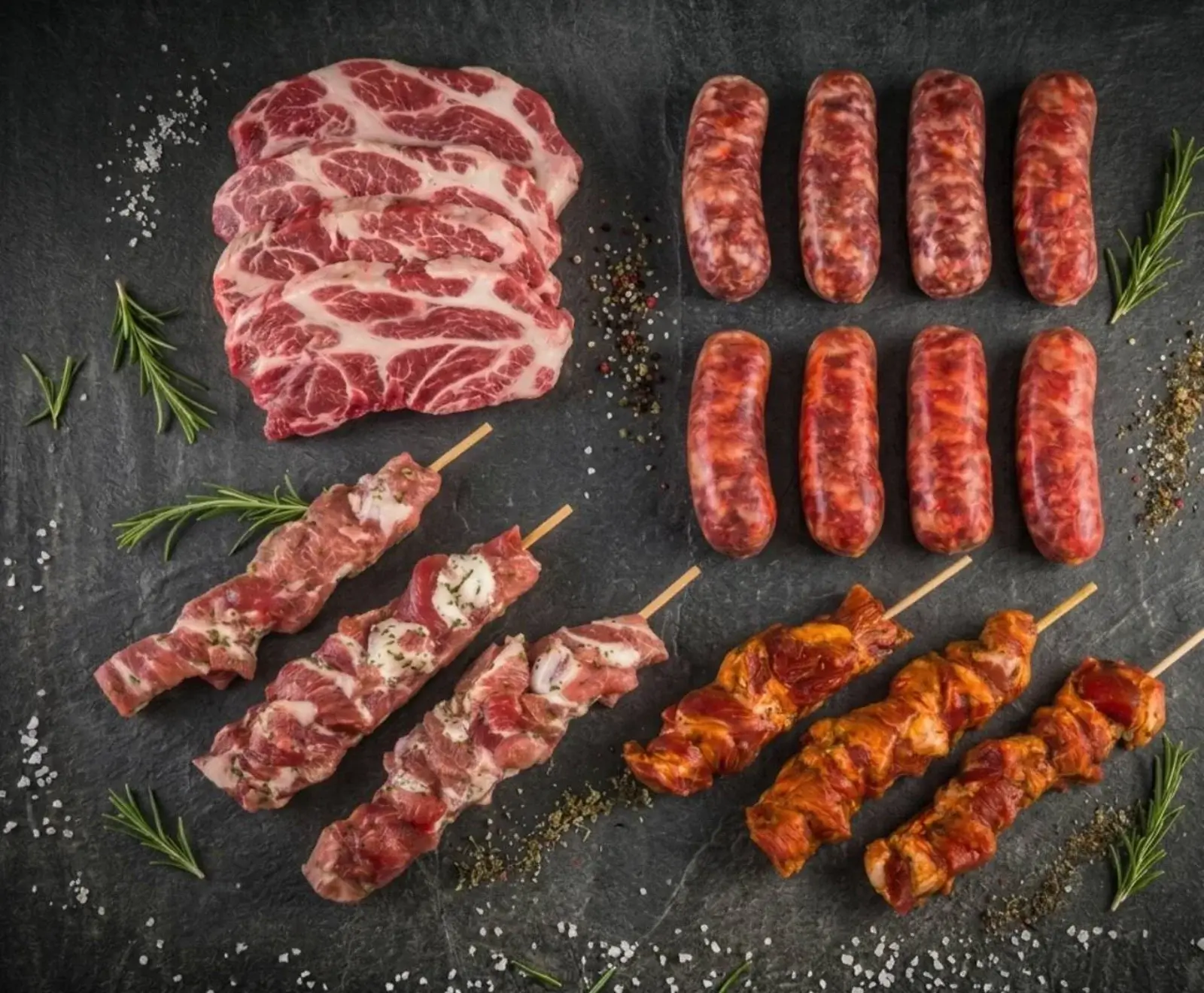 Eine Auswahl an rohem Fleisch auf dunklem Untergrund: gestapelte Nackensteaks, acht Bratwürste, drei unmarinierte und drei marinierte Fleischspieße, umgeben von Gewürzen und Rosmarin.