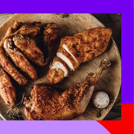 Nahaufnahme von verschiedenen Stücken gebratenem Hähnchen auf einem Holzbrett, darunter Flügel, eine aufgeschnittene Brust und ein Schenkel, garniert mit Kräutern.