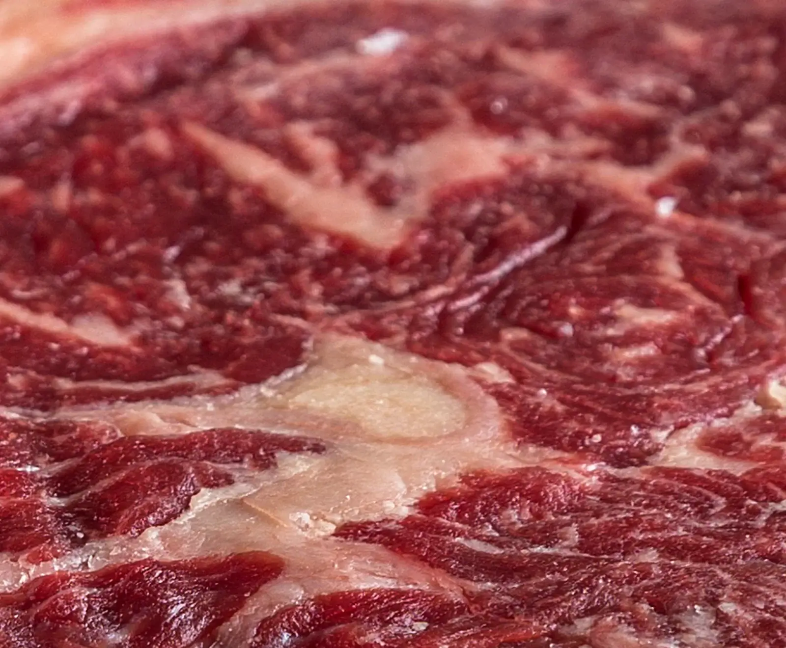 Nahaufnahme von marmoriertem Rindfleisch Nahaufnahme von rohem Rindfleisch mit ausgeprägter Marmorierung, die rote Muskelfasern und weiße Fettadern zeigt.