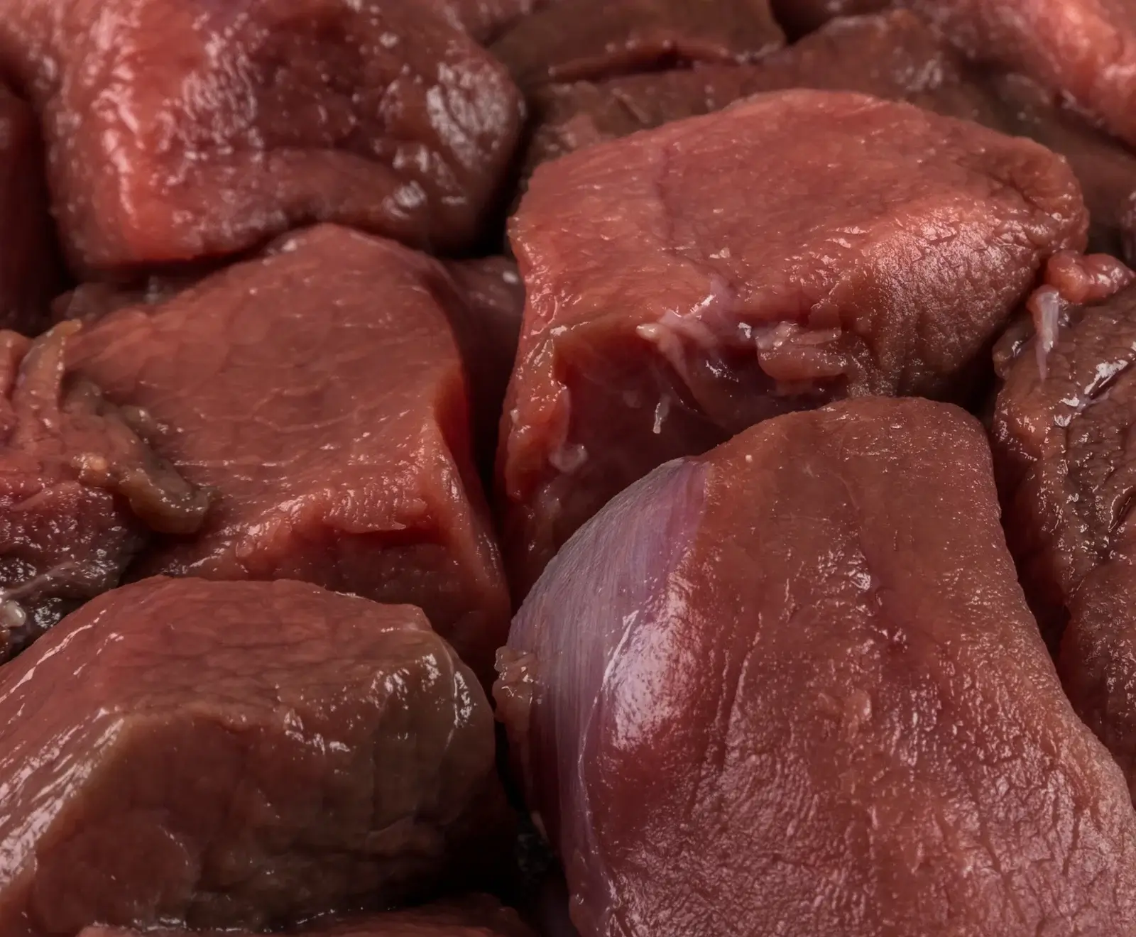 Nahaufnahme von rohen, dunkelroten Fleischstücken, die dicht beieinander liegen. Die Oberfläche ist leicht feucht und glänzend, mit sichtbaren Muskelfasern und etwas Bindegewebe.