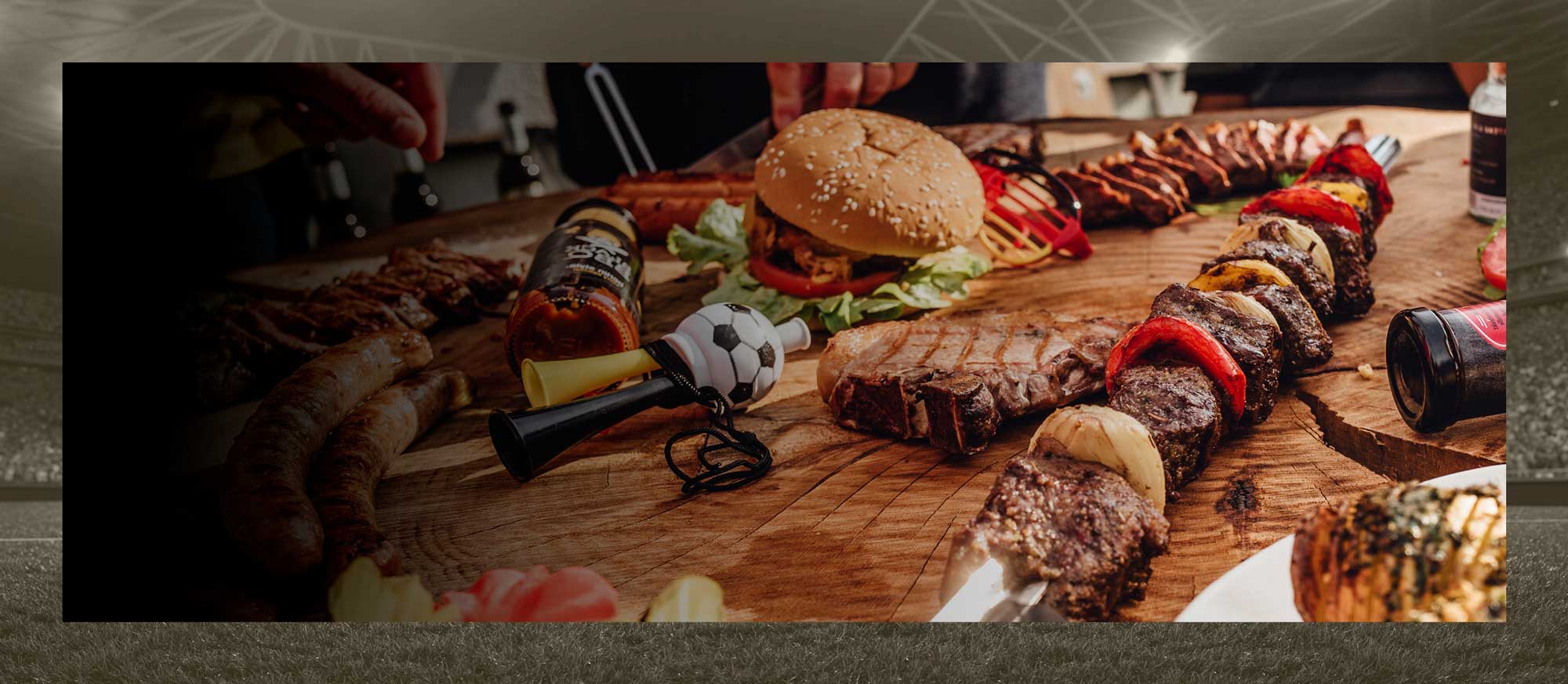 Gegrilltes Fleisch, Burger und Fußballdeko auf einem Tisch.