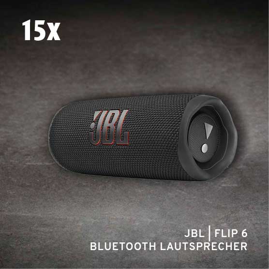 Ein schwarzer JBL Flip 6 Bluetooth-Lautsprecher liegt horizontal auf einem dunklen, strukturierten Hintergrund. Das JBL-Logo ist auf dem Stoffgitter zu sehen, und ein passiver Radiator mit Ausrufezeichen-Symbol ist an einem Ende sichtbar. Oben links steht