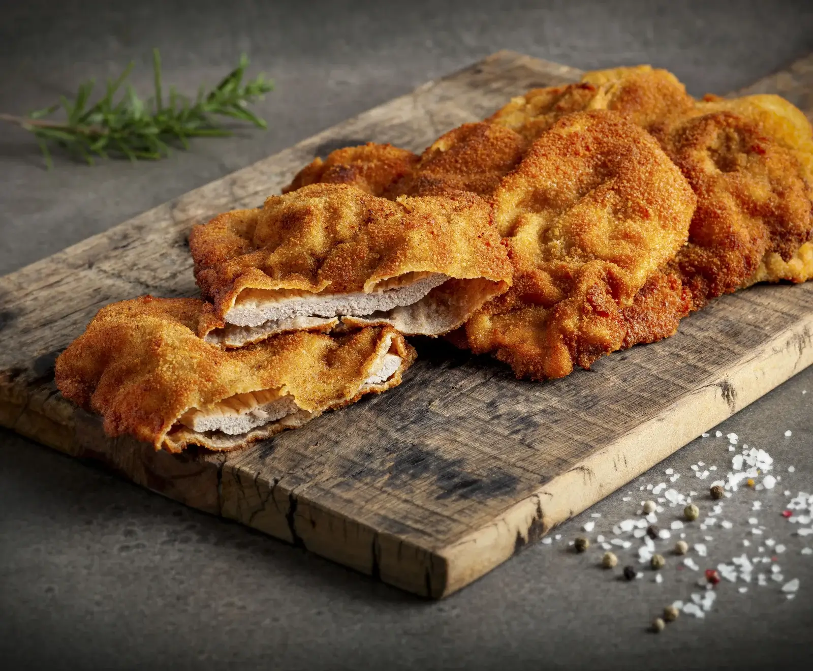 Knusprige panierte Hühnchenschnitzel auf einem Holzbrett, garniert mit Rosmarin und Salz