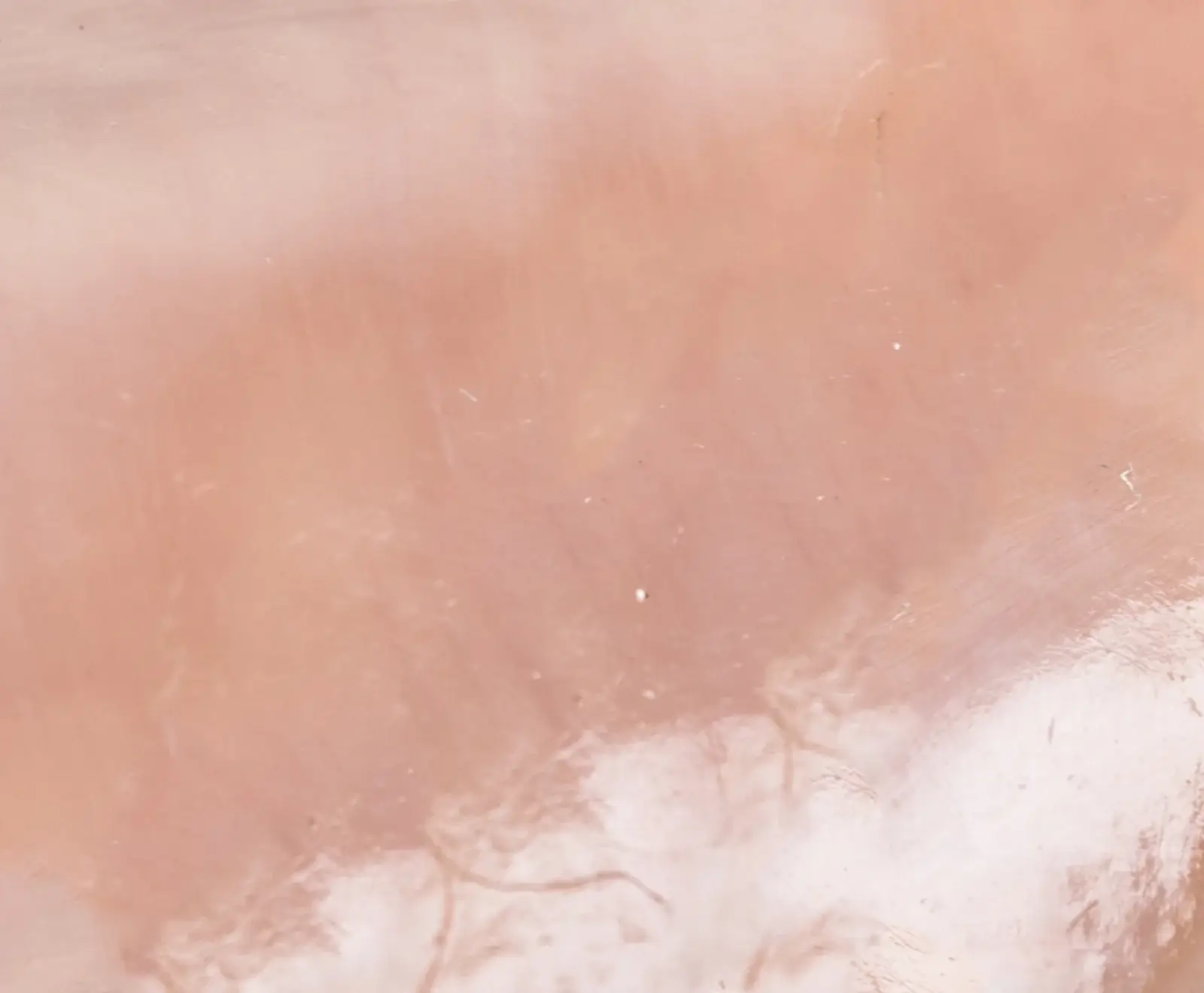 Nahaufnahme einer glatten, durchscheinenden Oberfläche in zartem Rosé, die an Rosenquarz erinnert. Sie zeigt subtile Farbverläufe, feine Linien und organisch wirkende Strukturen im unteren Bereich.