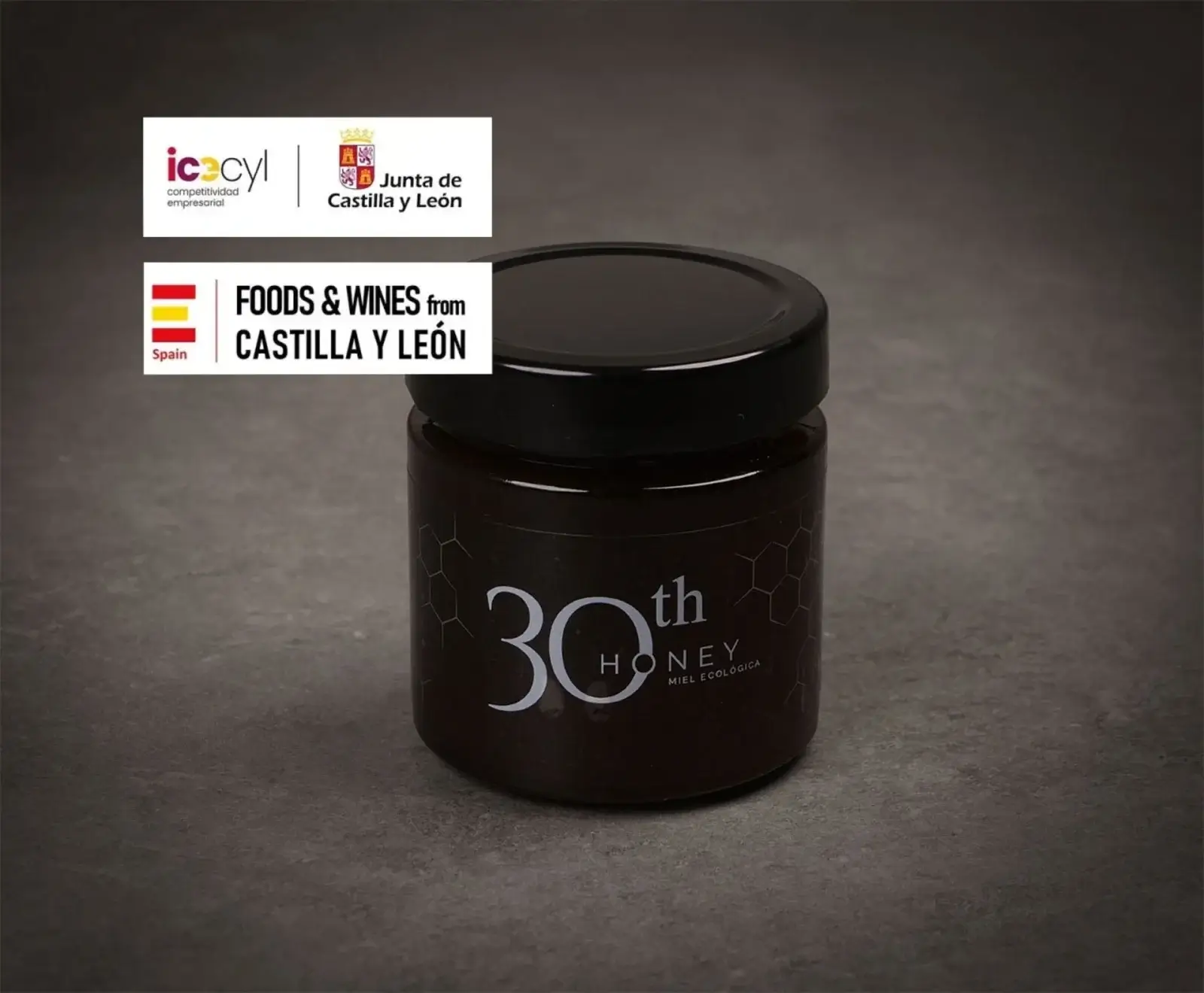 Dunkles Honigglas mit schwarzem Deckel, beschriftet mit "30th HONEY MIEL ECOLÓGICA" und Wabenmuster. Oben links Logos von ICECYL, Junta de Castilla y León und "Foods & Wines from Castilla y León".