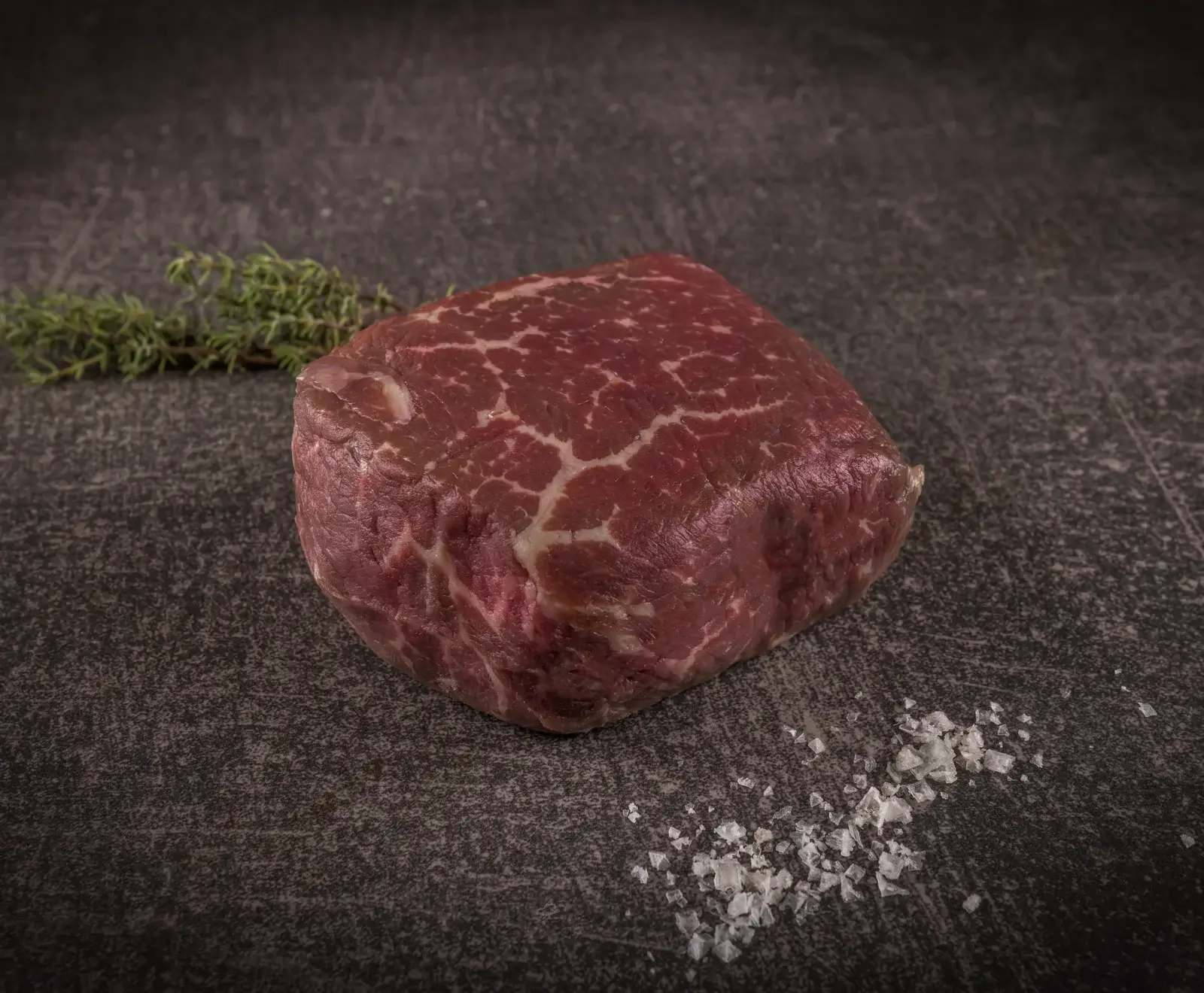 Ein rohes Rinderfilet-Steak auf einer dunklen Schieferplatte, garniert mit Thymian und Salz.