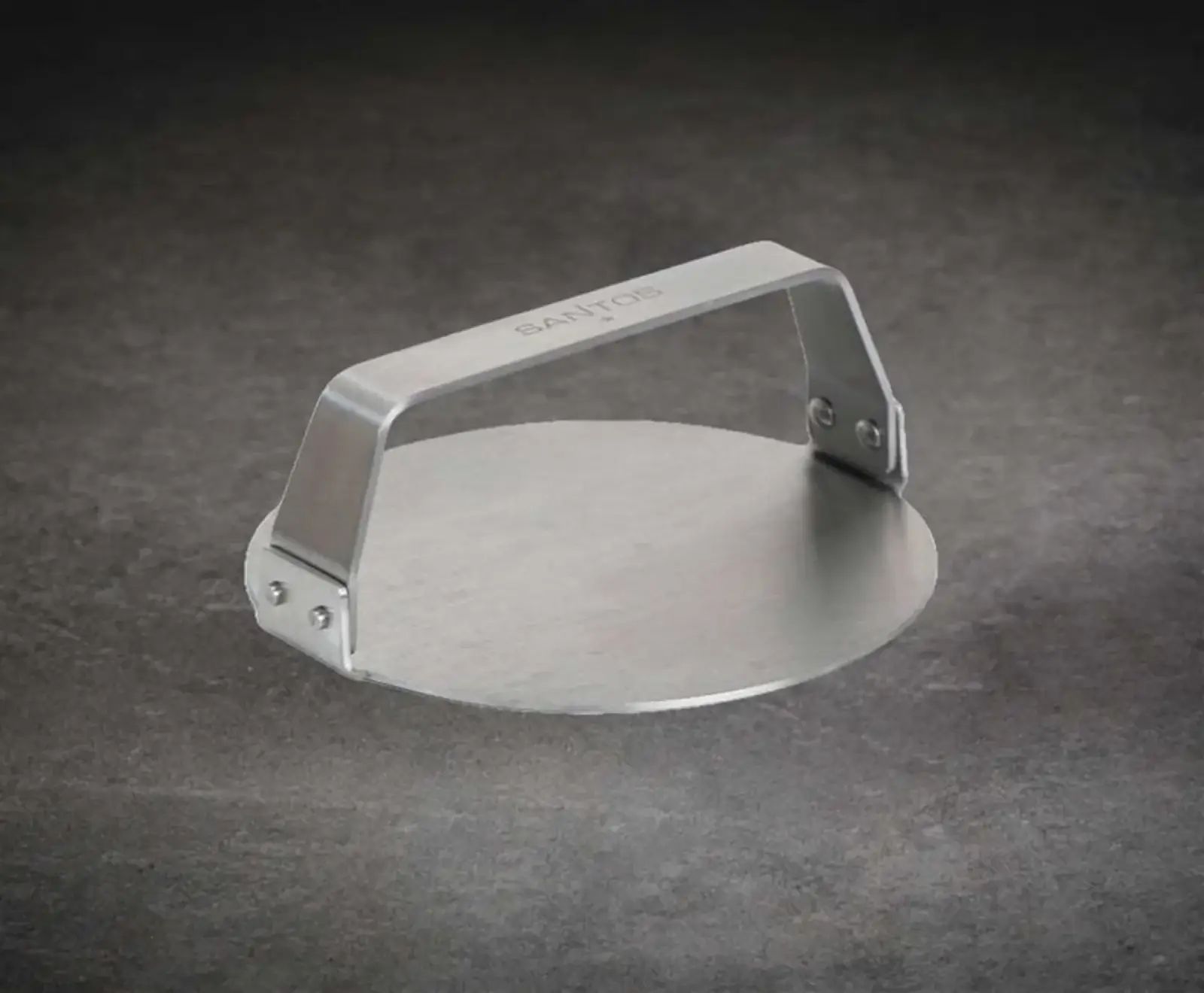 Eine runde Burgerpresse aus gebürstetem Edelstahl mit einem Griff und dem "SANTOS"-Logo, auf einem dunklen, strukturierten Hintergrund.