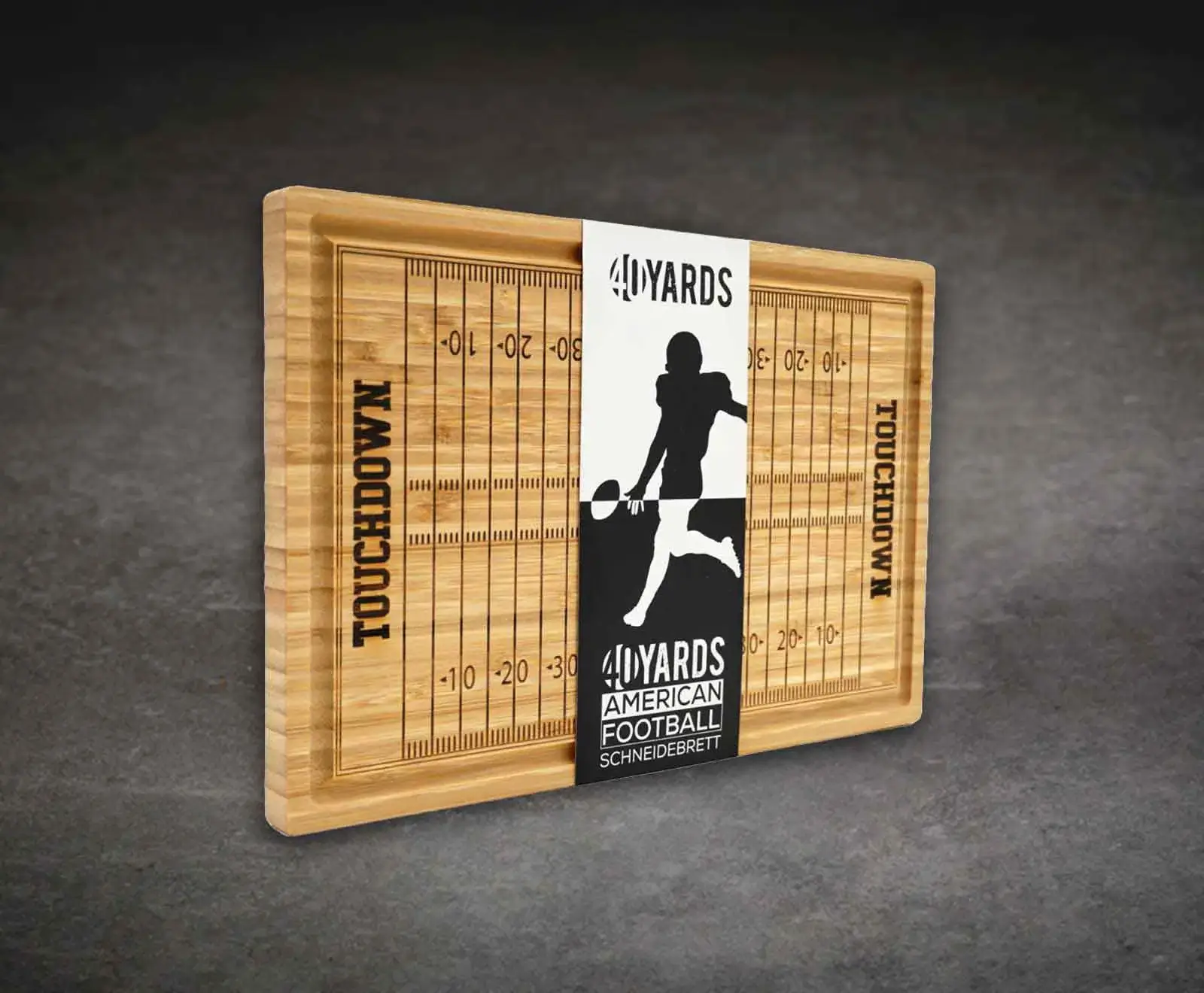 Ein rechteckiges Schneidebrett aus hellem Holz mit einem eingravierten American Footballfeld-Design, inklusive Yard-Linien und "TOUCHDOWN" an den Enden. Eine Banderole mit einem Footballspieler-Schattenbild und dem Text "40 YARDS AMERICAN FOOTBALL SCHNEID