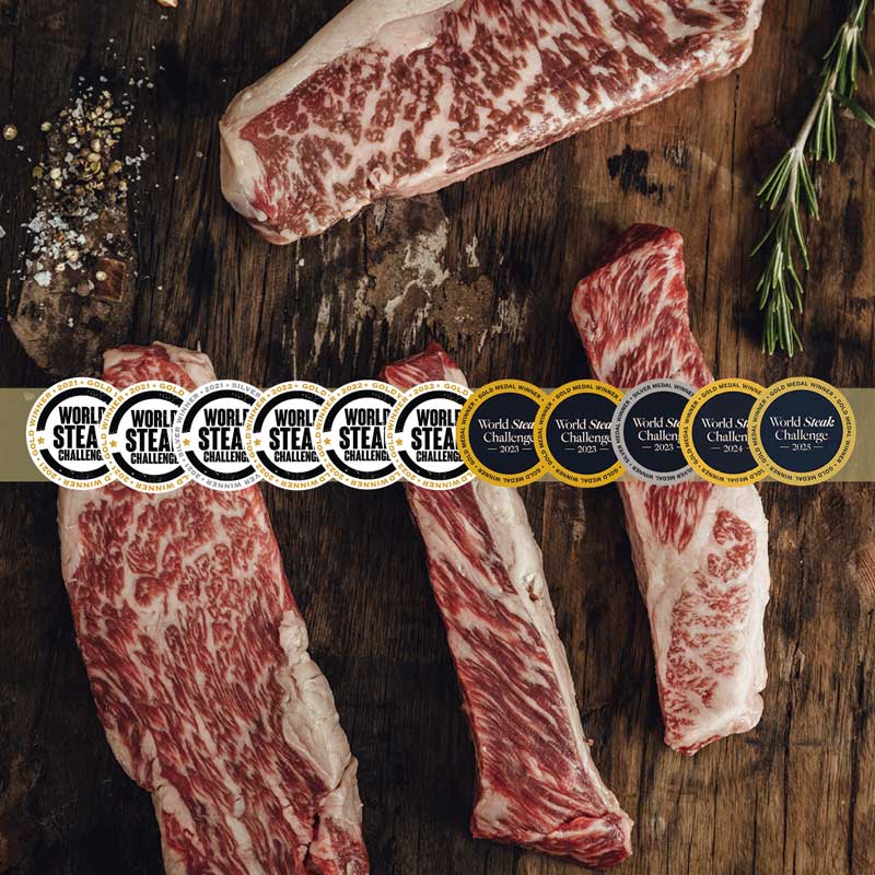 Rohe, stark marmorierte Steaks auf Holzbrett mit Gewürzen und Rosmarin, überlagert von Gold- und Silbermedaillen der "World Steak Challenge" von 2021 bis 2025.
