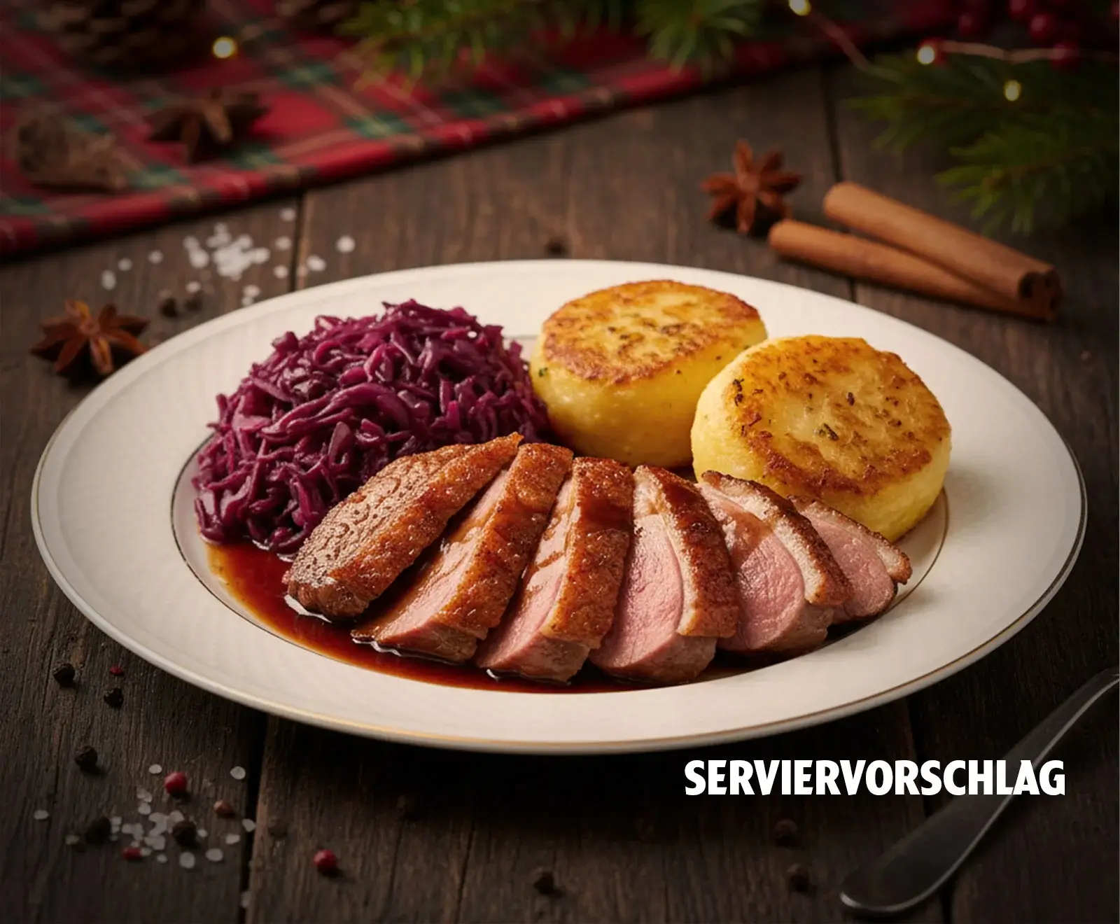 Auf einem Holztisch angerichteter Teller mit geschnittener Entenbrust, Rotkohl und zwei Kartoffelpuffern, umgeben von weihnachtlicher Dekoration. Text: SERVIERVORSCHLAG.