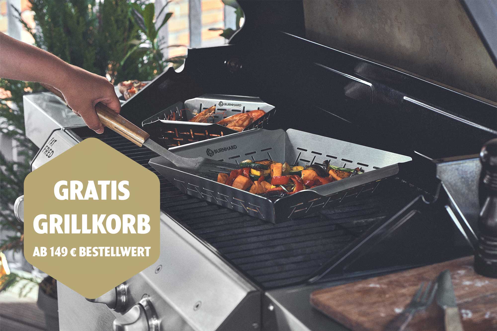 Eine Hand rührt mit einem Pfannenwender Gemüse in einem Burnhard Grillkorb auf einem Gasgrill. Ein zweiter Korb mit Garnelen ist im Hintergrund. Ein goldener Hinweis bietet einen gratis Grillkorb ab 149 € Bestellwert.