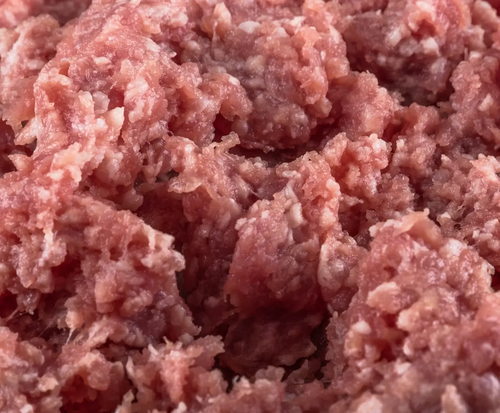 Nahaufnahme von frischem, rohem Hackfleisch, das aus rosa Fleischstücken und weißen Fettpartikeln besteht. Die Textur ist grob und unregelmäßig.