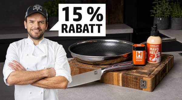 Der lächelnde Koch Steffen Henssler in weißer Uniform und Kappe steht mit verschränkten Armen. Rechts sind ein Wok, ein Messer, Gewürz und Mayo auf einem Holzbrett zu sehen. Ein Banner zeigt "15 % RABATT".