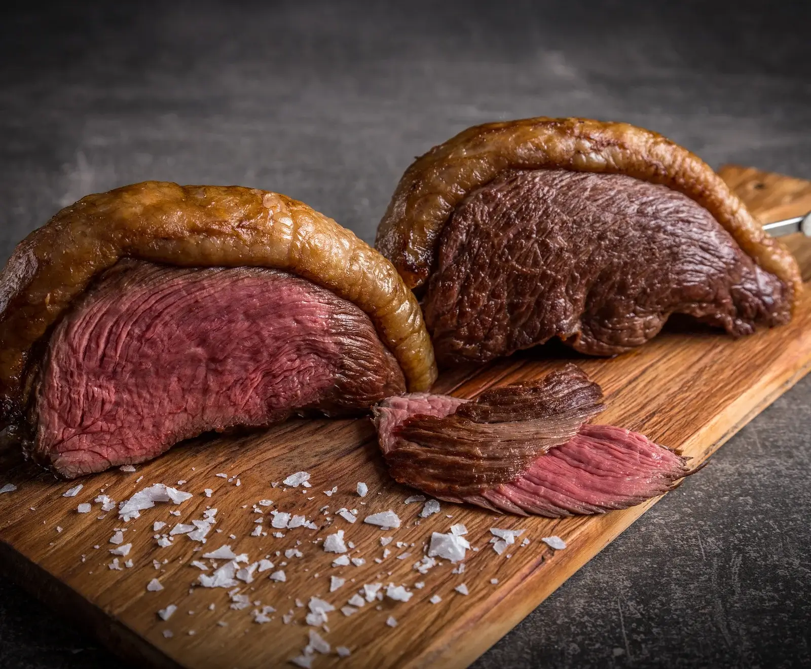 Zwei Scheiben saftiges, medium-gegrilltes Steak auf einem Holzbrett mit Salz daneben.