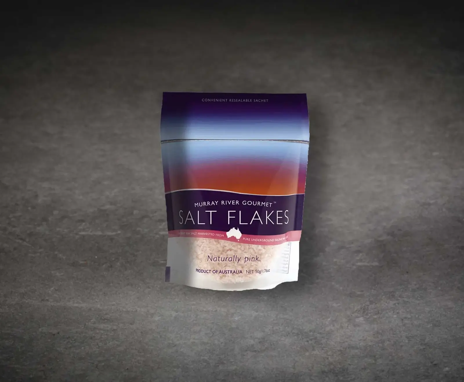 Stehender Beutel Murray River Gourmet Salzflocken auf dunklem Hintergrund. Die lila-orange Verpackung zeigt durch einen transparenten Bereich die natürlich rosa Salzflocken. Beschriftung: „Naturally pink“.