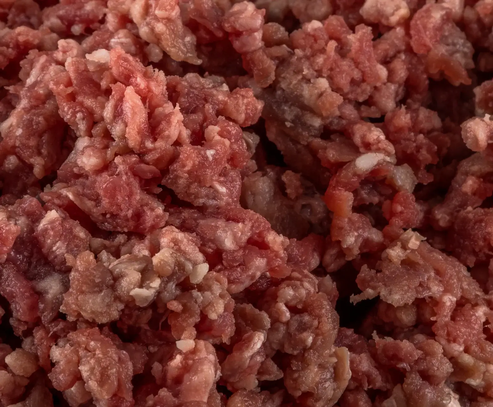 Nahaufnahme von rohem, grob gehacktem Hackfleisch mit sichtbaren Fettanteilen, das eine rötliche Farbe aufweist und die gesamte Bildfläche füllt.