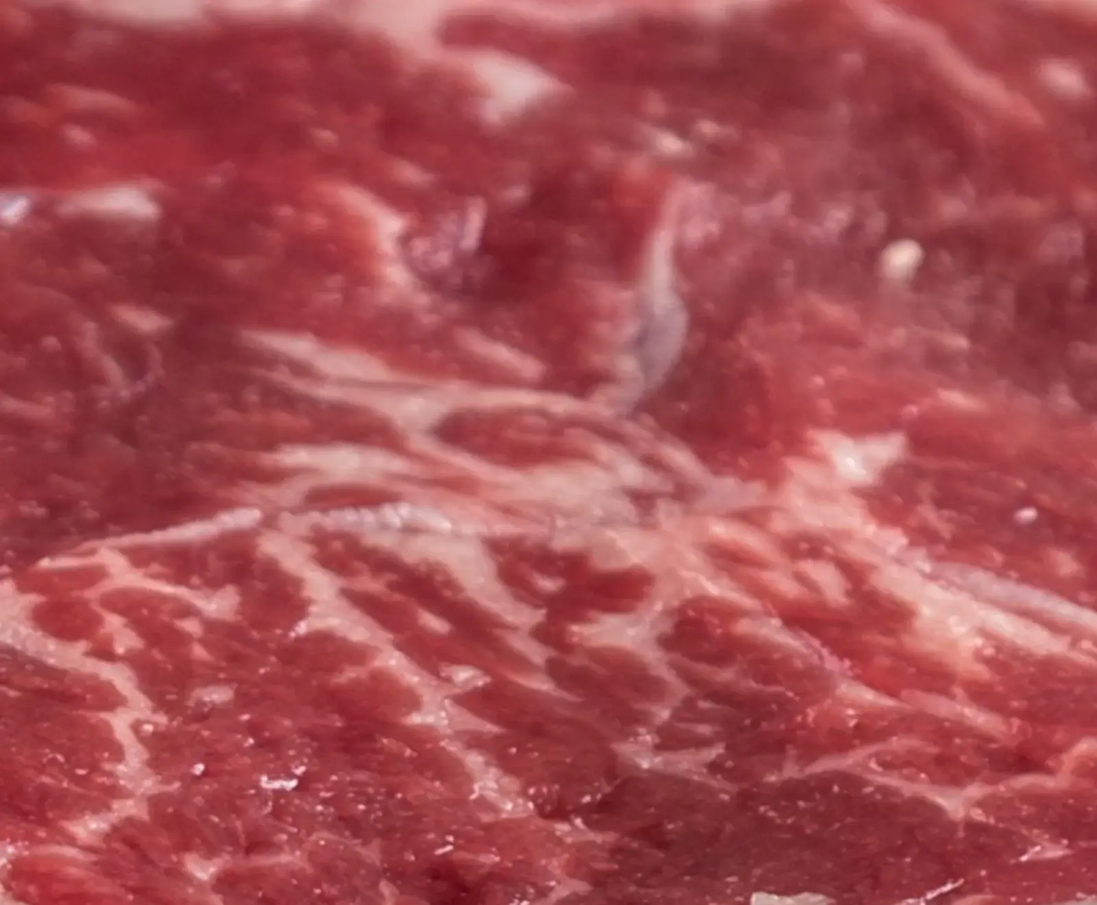 Nahaufnahme von rotem, rohem Fleisch mit deutlicher weißer Marmorierung (Fettadern), die eine feine Netzstruktur bildet. Die Oberfläche ist leicht glänzend.