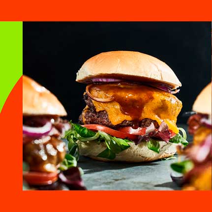Nahaufnahme eines saftigen Doppel-Cheeseburgers mit geschmolzenem Käse, dunkler Sauce, roten Zwiebeln, Salat und Tomate auf einem Brötchen. Unscharfe Burger links und rechts.