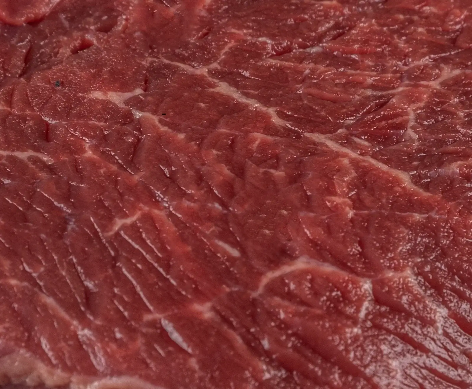 Nahaufnahme von rohem, dunkelrotem Fleisch mit sichtbaren Muskelfasern und feiner weißer Marmorierung.
