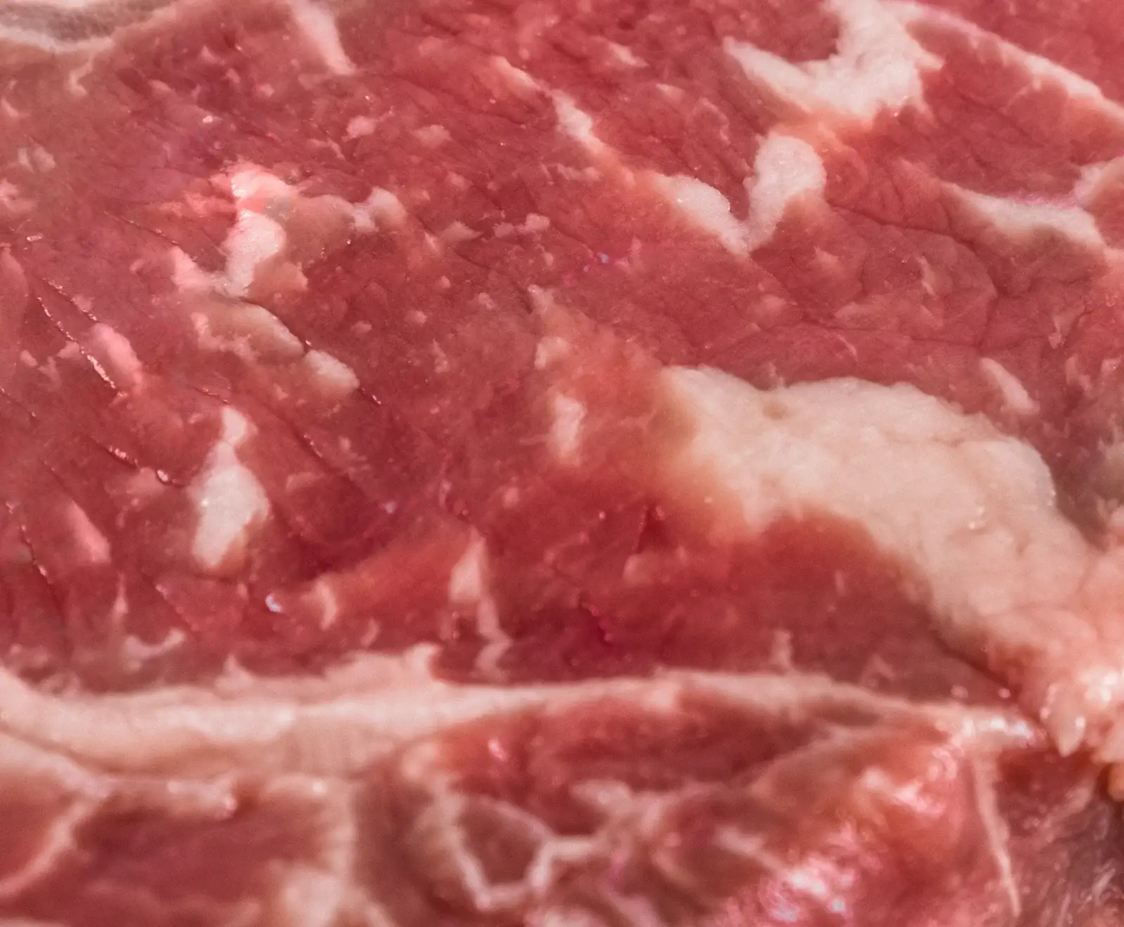 Nahaufnahme von rotem Fleisch mit deutlicher weißer Fettmarmorierung, die die Textur des rohen Steaks zeigt.