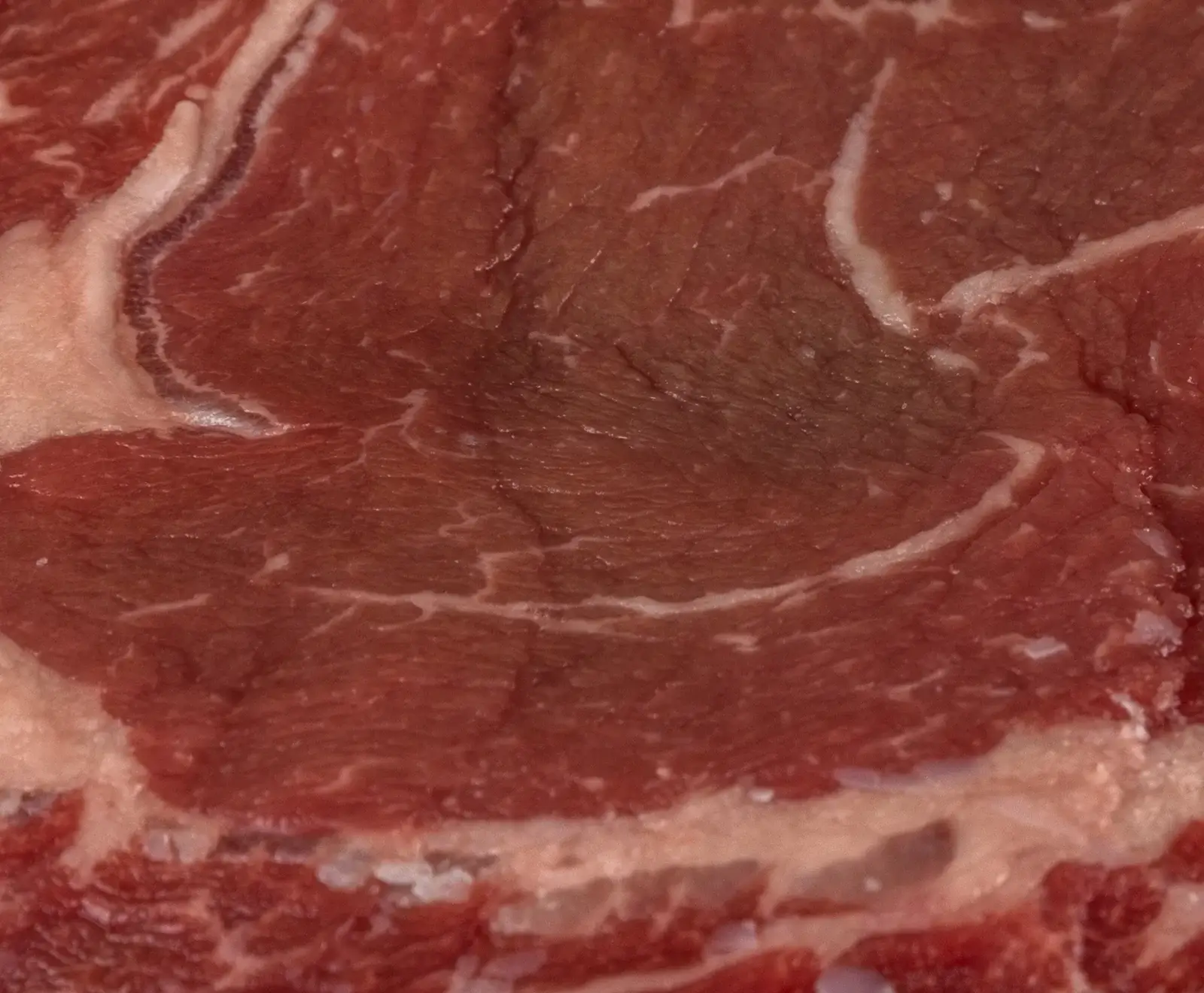 Nahaufnahme von rotem, rohem Fleisch mit deutlicher weißer Marmorierung und Fettstreifen, die sich durch das Muskelgewebe ziehen.